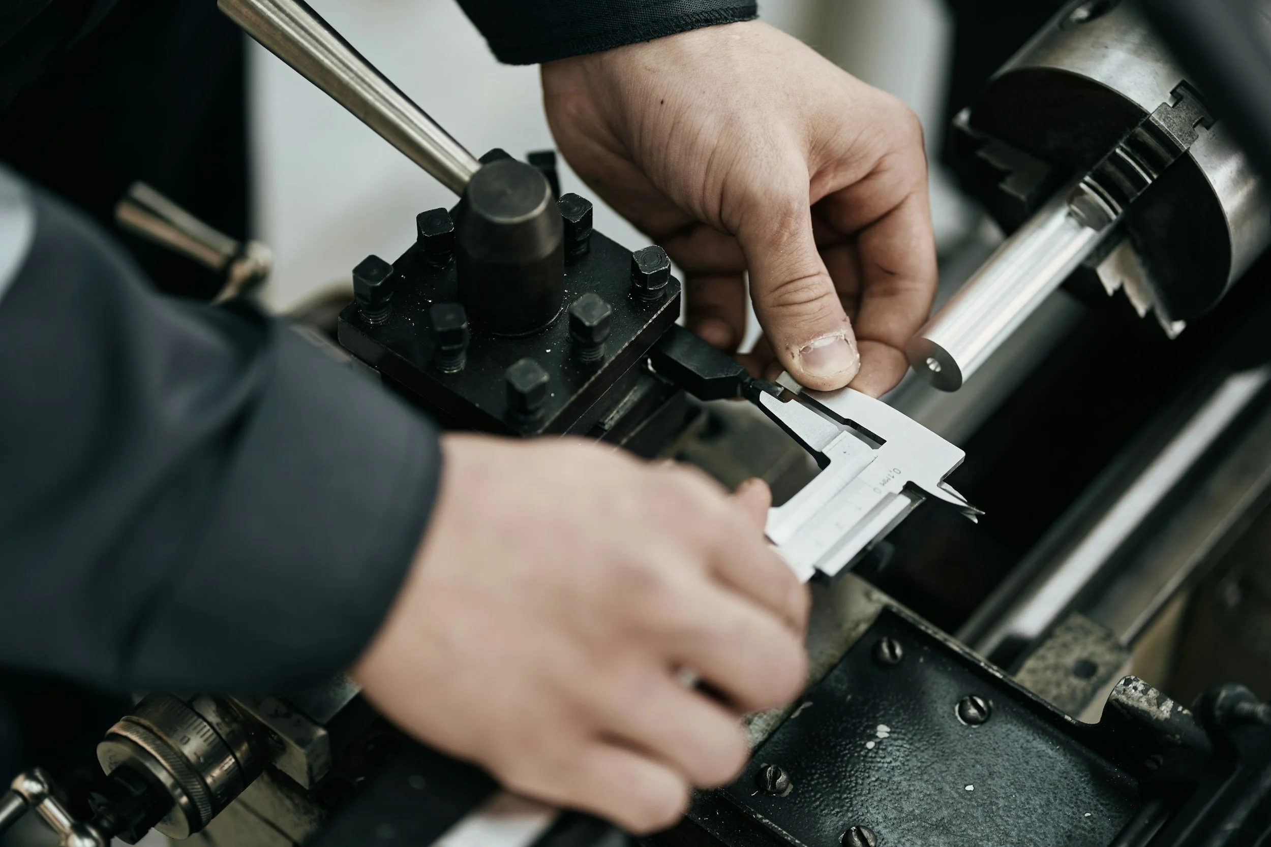Close-up of a person's hands working on a metal machine or tool, possibly part of a mechanical or manufacturing process.