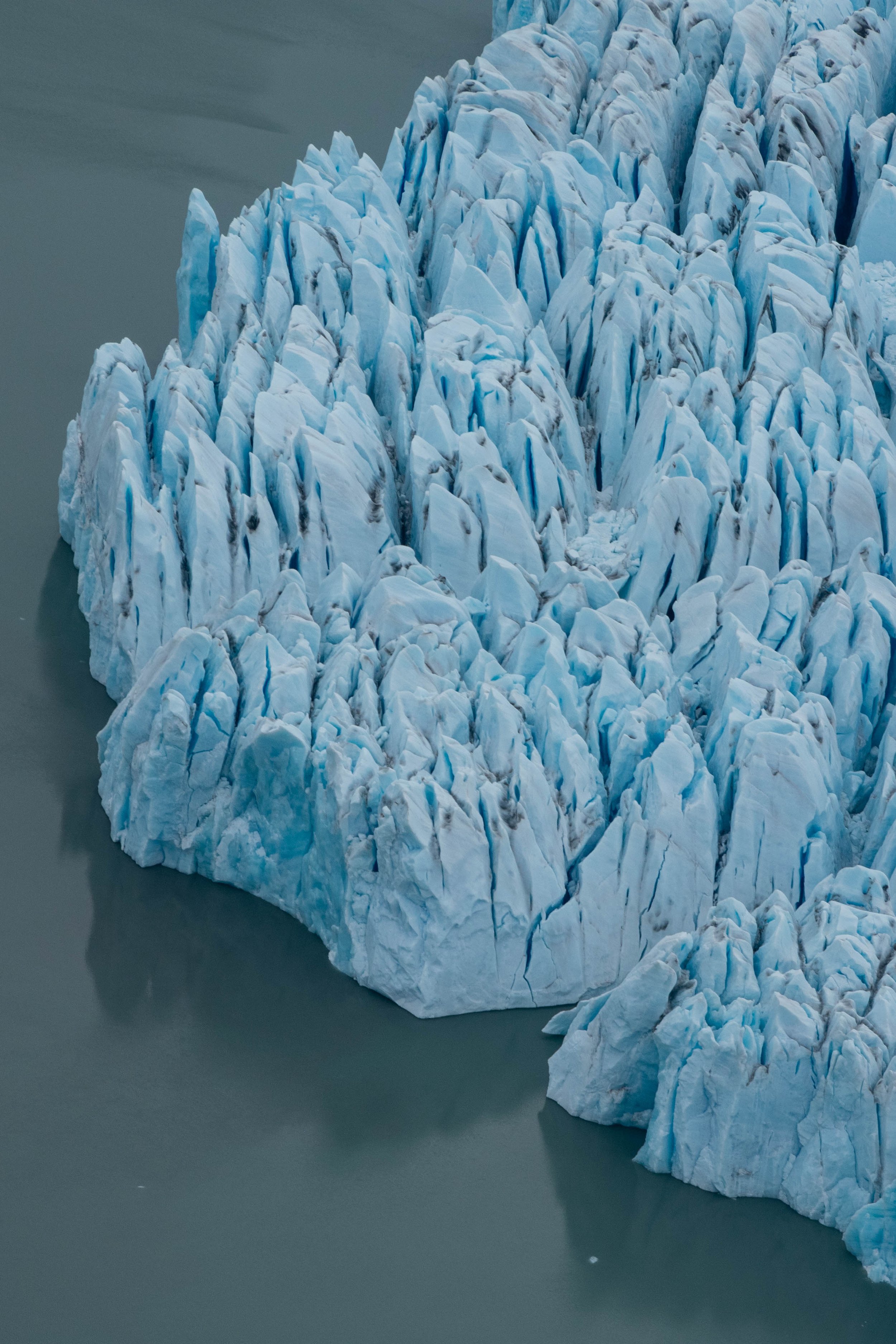 Close-up view of a glacier with jagged ice formations and a dark water body surrounding it.