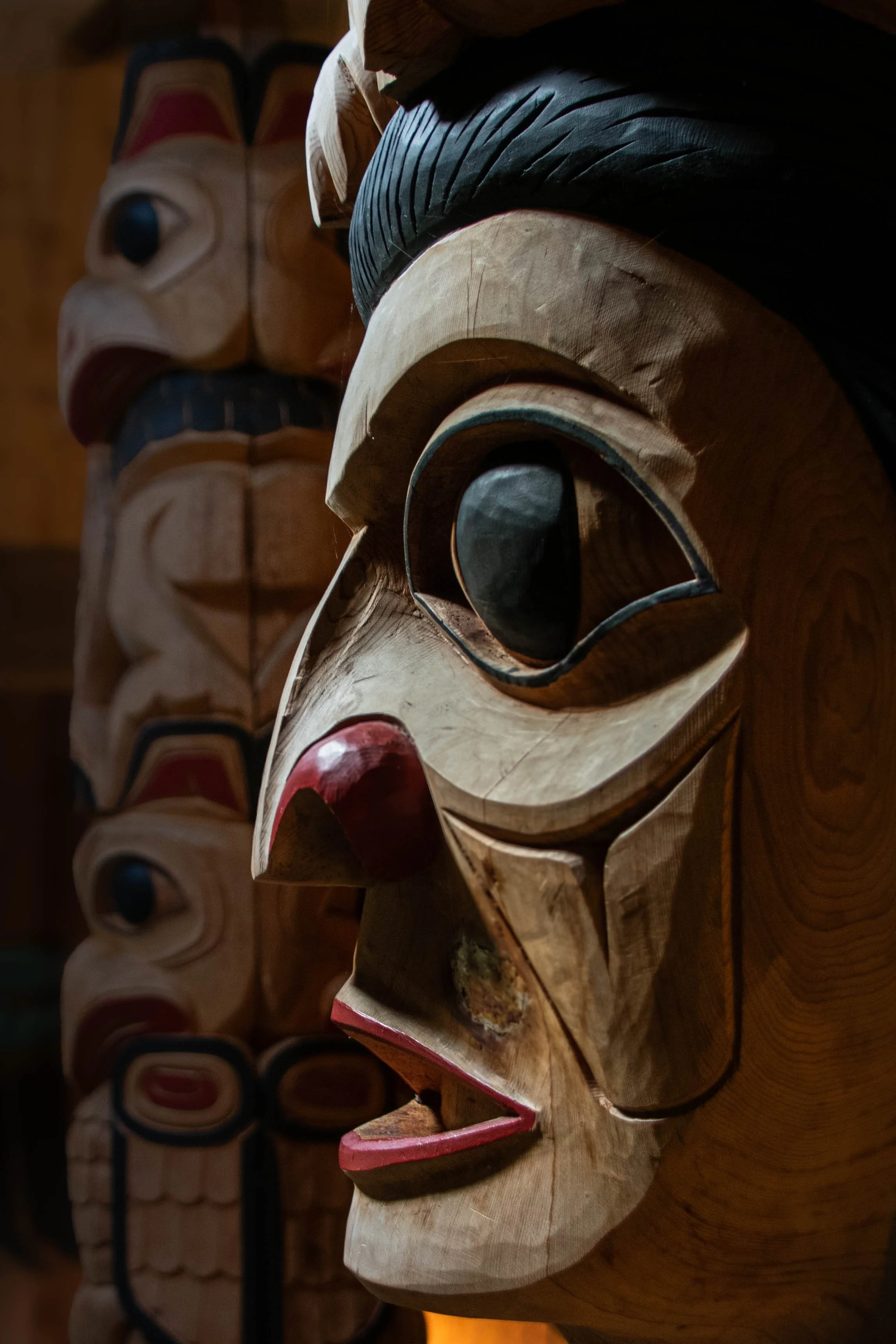 Close-up of a traditional wooden mask with carved features and painted accents, displayed among other similar masks.