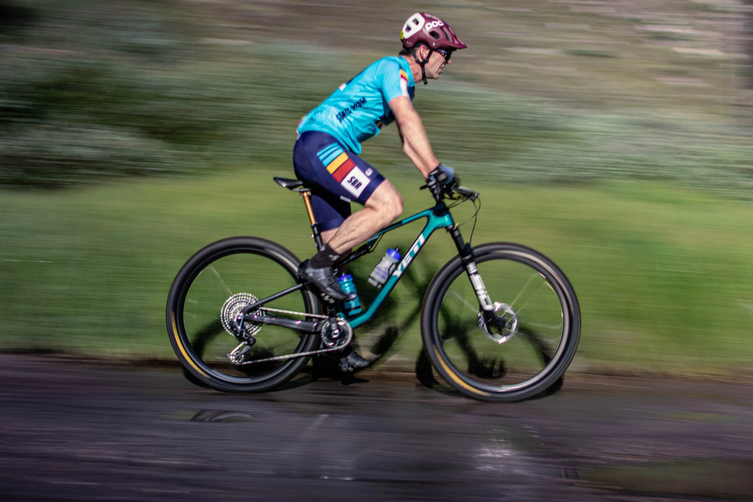 A man riding a mountain bike on a trail with motion blur and greenery in the background.