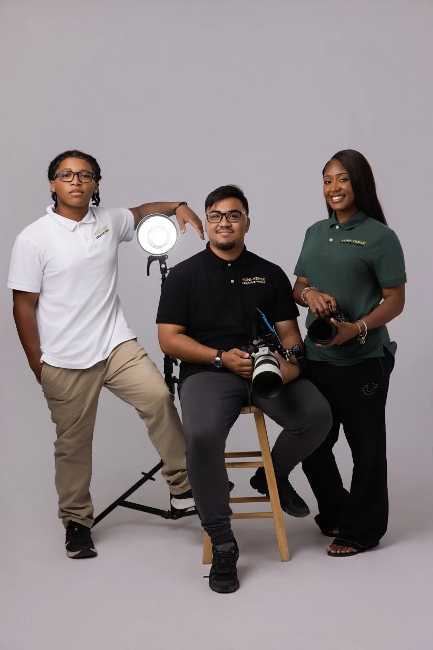 Three diverse people in a studio with photography equipment, including a large camera and a light, posing for a photo.