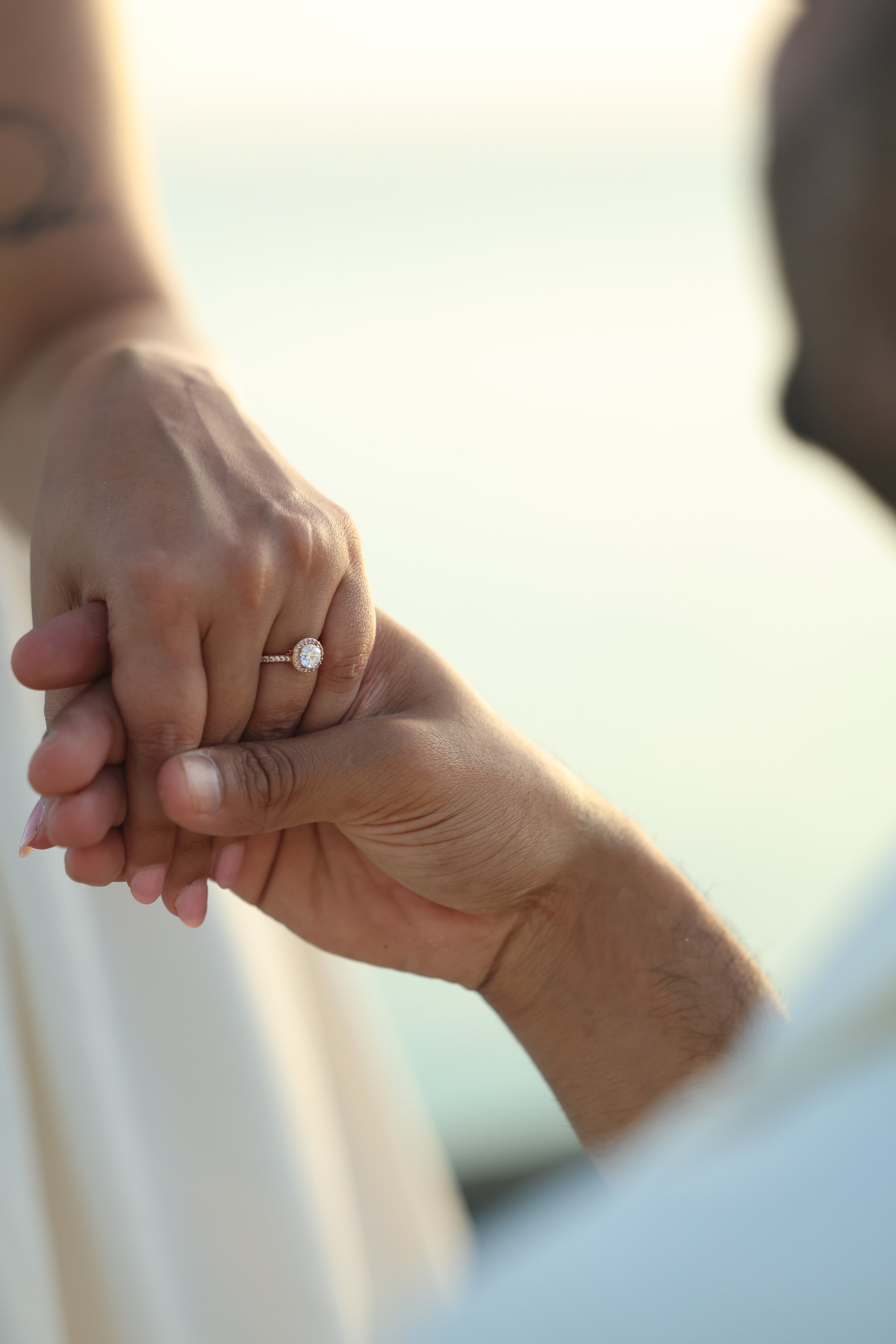 A close-up of a person holding hands with another person, showing an engagement ring with a large diamond on the ring finger.