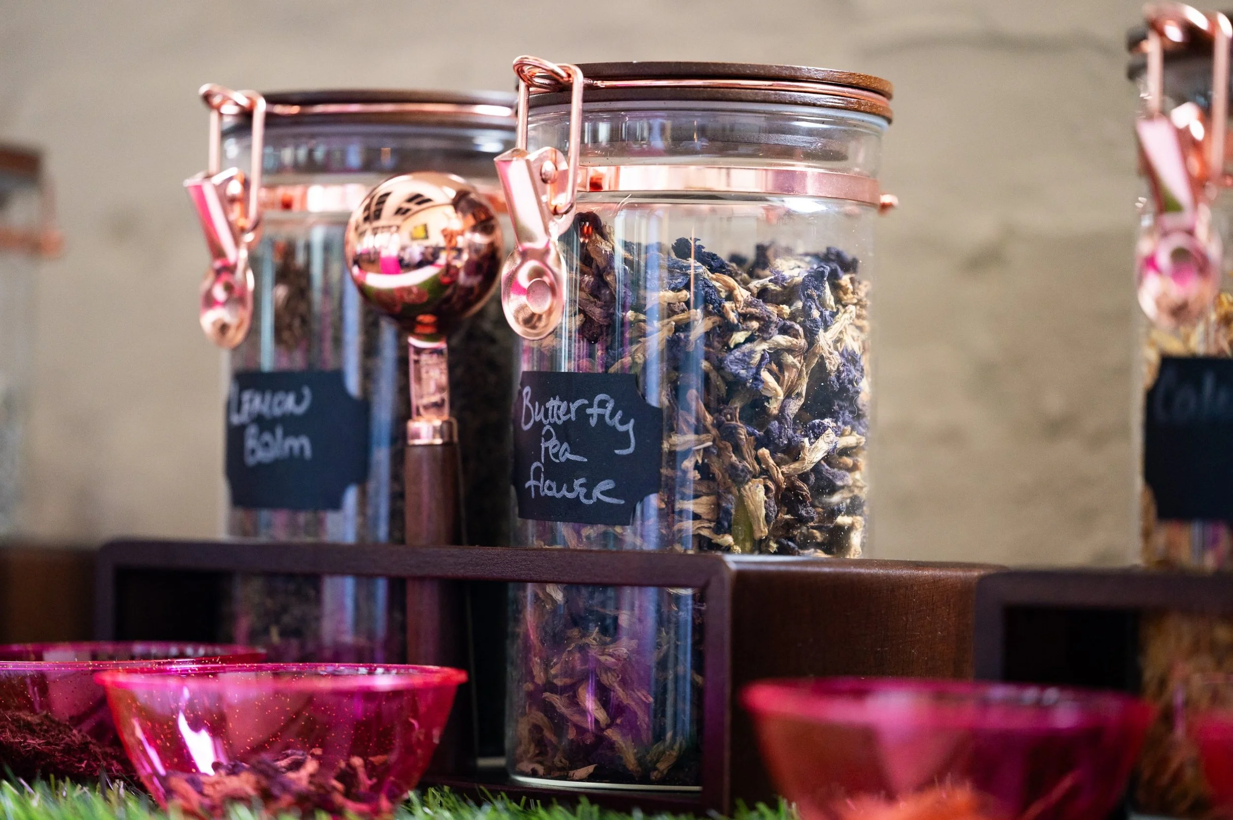 Glass apothecary jars of lemon balm and butterfly pea flower with rose-gold scoops