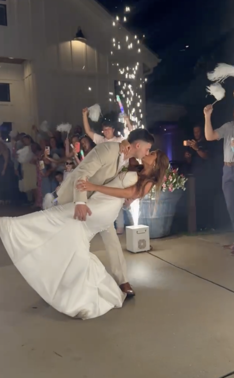 A newly married couple sharing a dance at their wedding reception, surrounded by guests, sparklers, and celebration lighting.