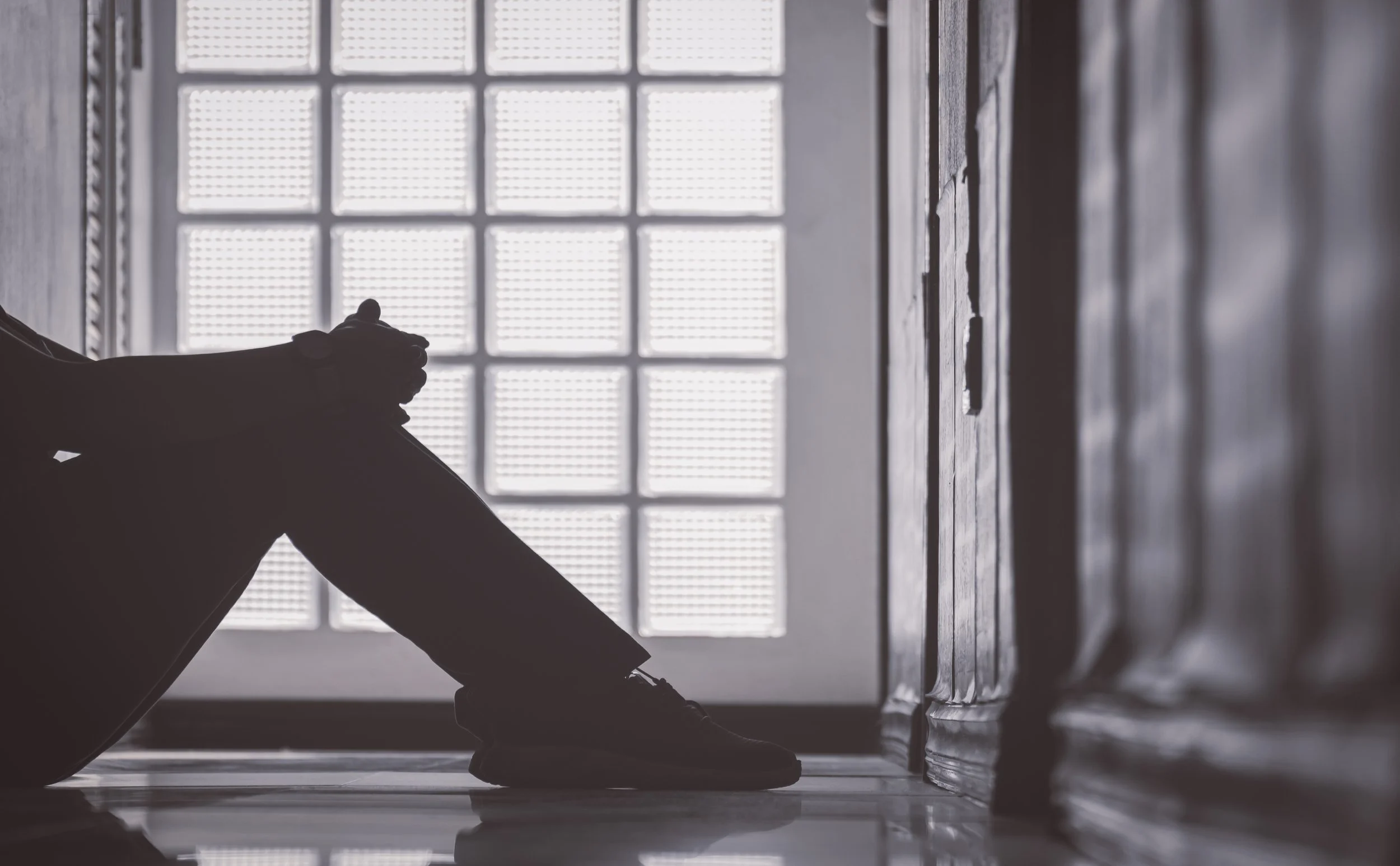 Silhouette of a person sitting on the floor next to a brick wall, with a large window in the background.