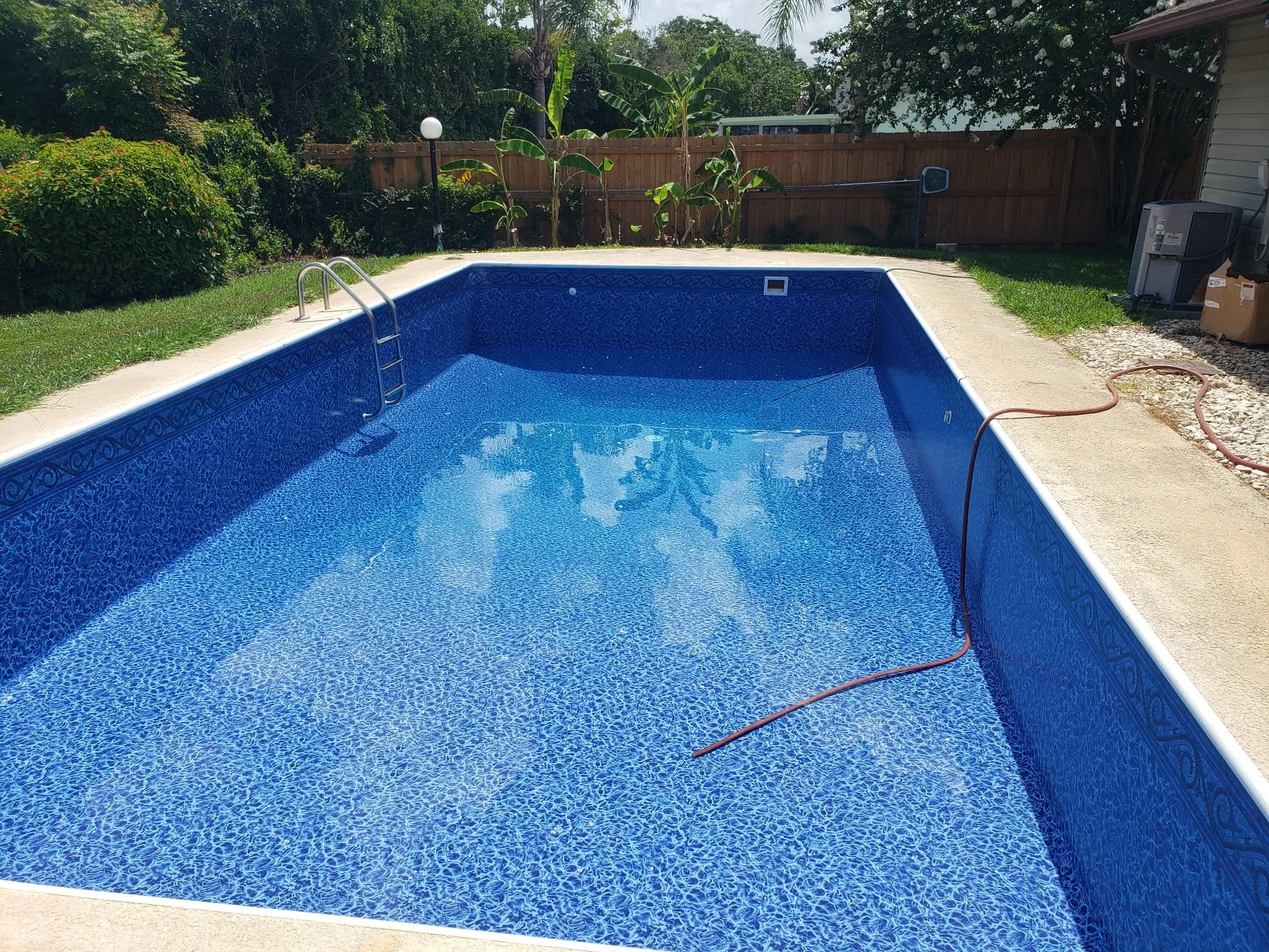 Rectangular inground swimming pool with blue liner and metal ladder.