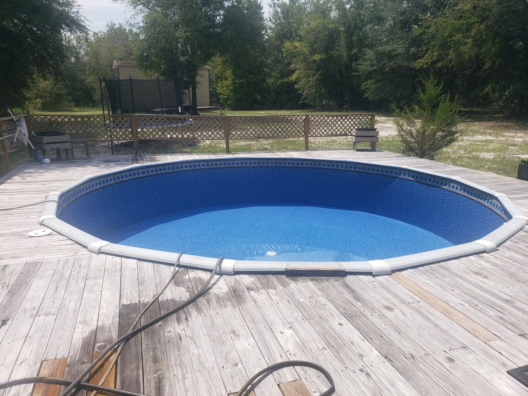 Completed round above-ground swimming pool with surrounding wooden deck.