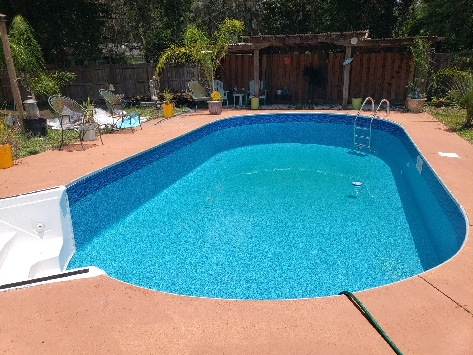 Inground swimming pool with blue liner, ladder and surrounding concrete deck.
