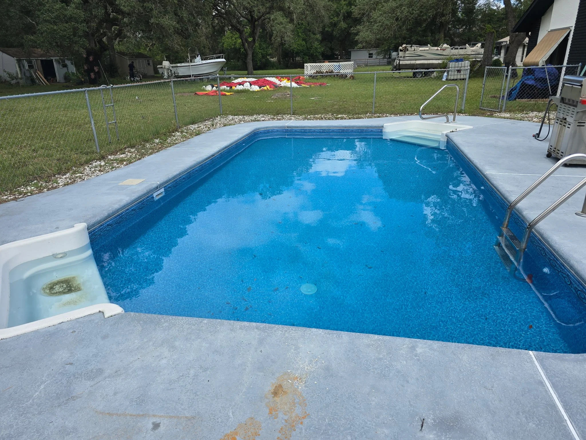 Completed inground swimming pool with blue liner, steps and metal handrails.