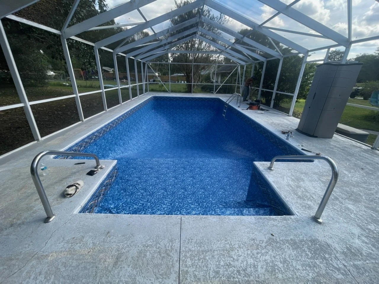 Inground pool liner replacement with blue liner inside a screened enclosure. 