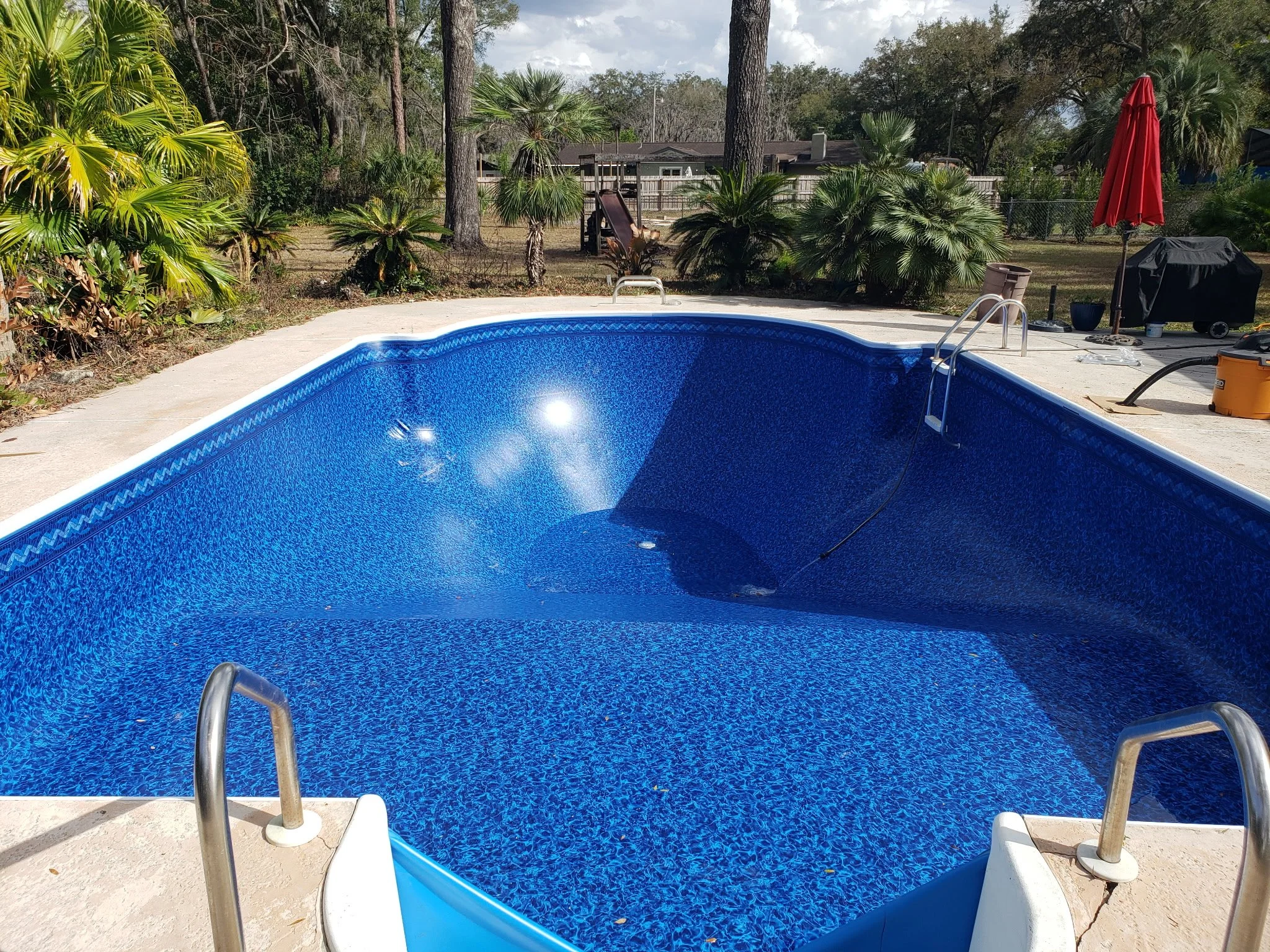 Completed inground swimming pool with blue liner and concrete pool deck.