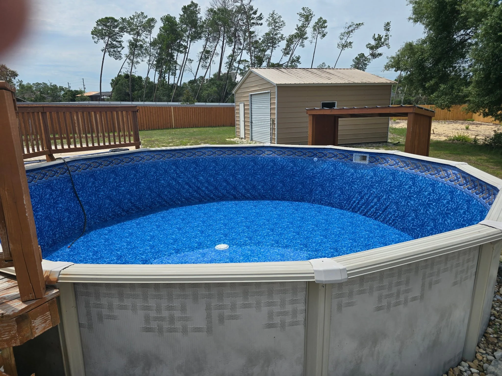 Above-ground swimming pool with blue liner and surrounding wooden deck.