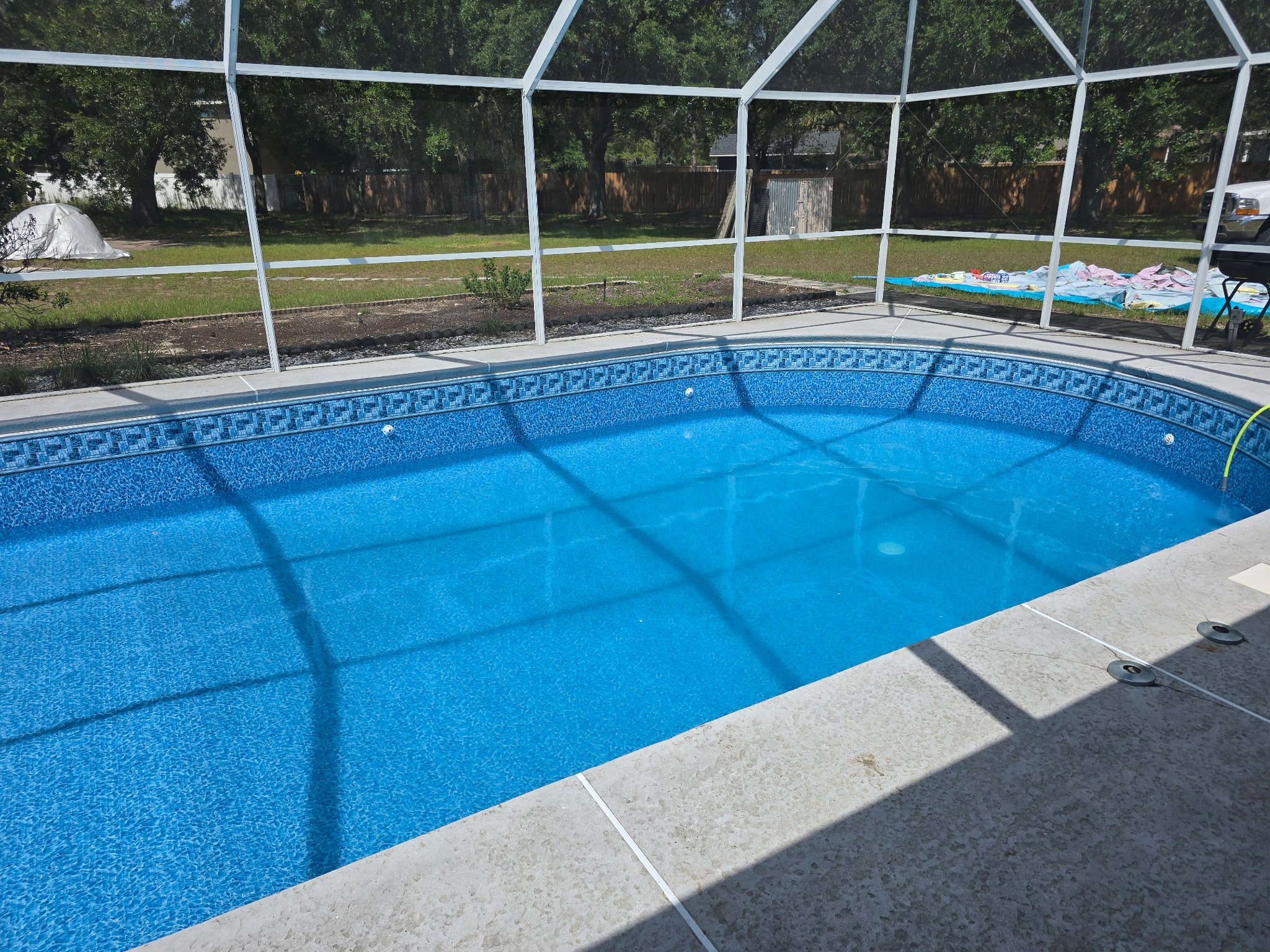 Inground swimming pool with blue liner inside a screened enclosure. 