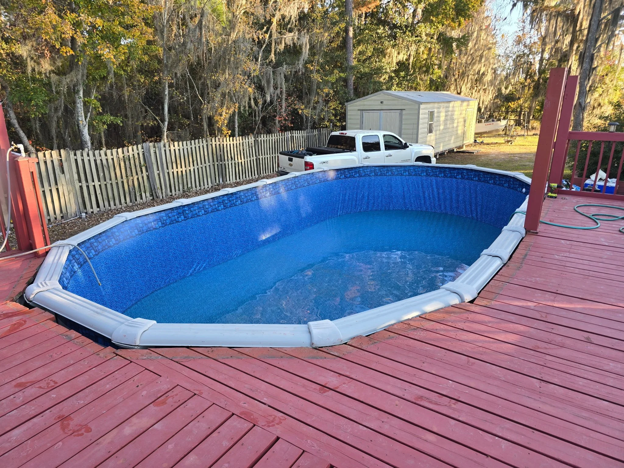 Comepleted above-ground swimming pool with blue liner and surrounding wooden deck.
