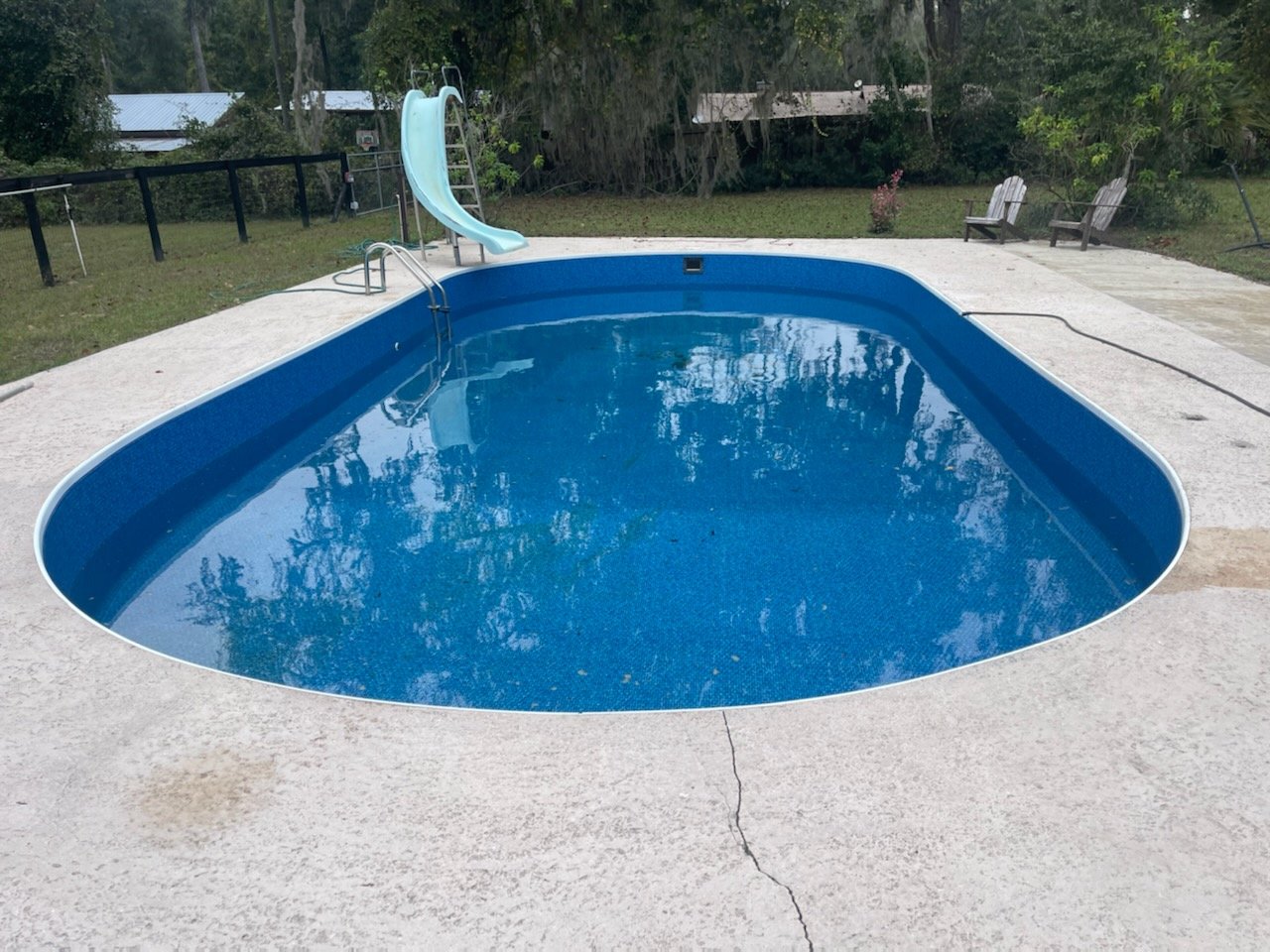 Inground swimming pool with blue liner, slide, and concrete pool deck.