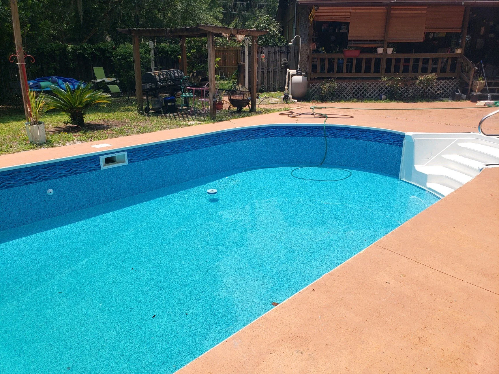Completed inground swimming pool with new blue liner and concrete pool deck.