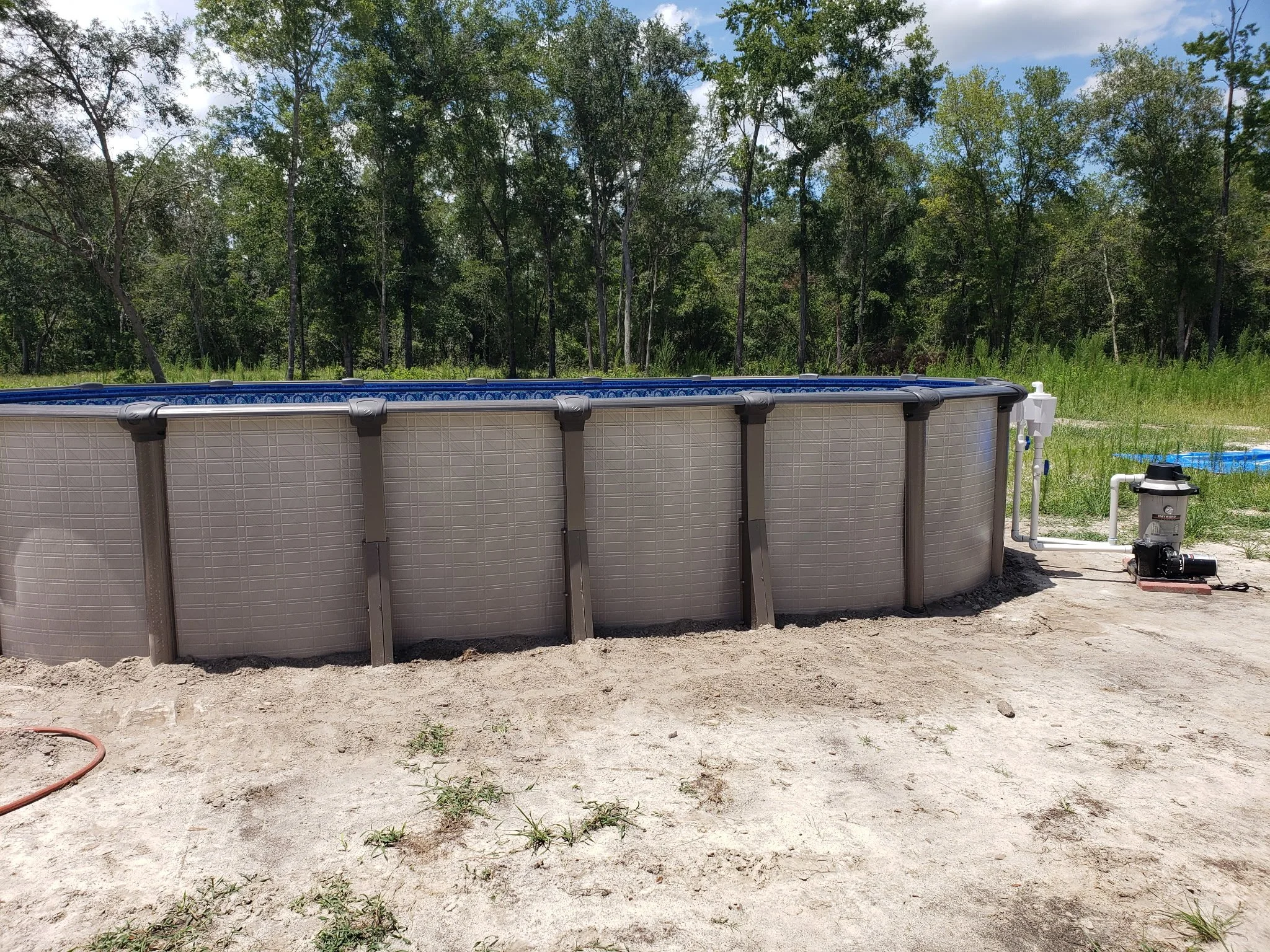Above-ground swimming pool installation with metal frame on prepared ground.