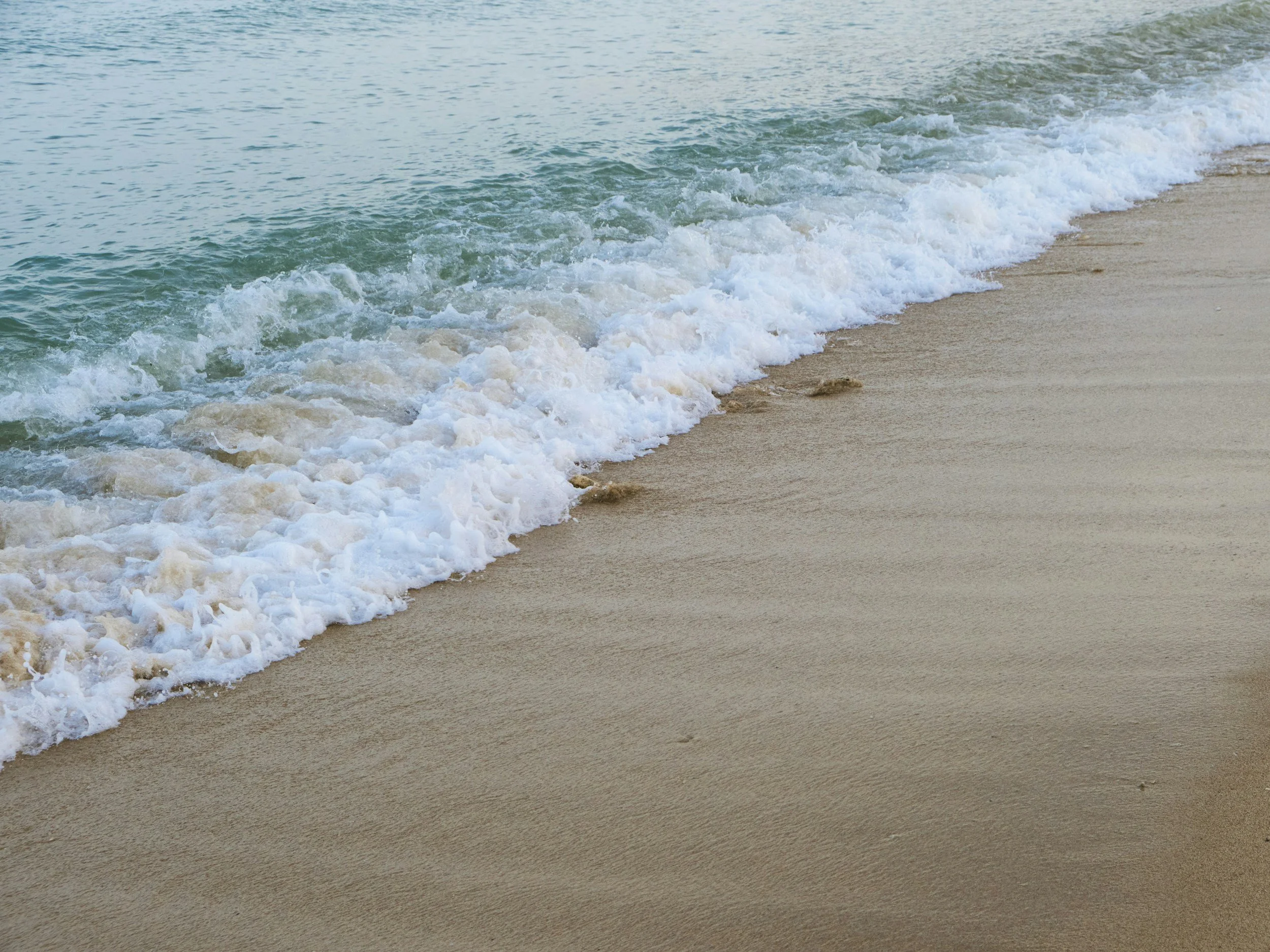 Peaceful waves gently lapping onto a sandy beach with light-colored sand and clear water, representing support, healing, and online therapy for OCD, anxiety, and trauma.