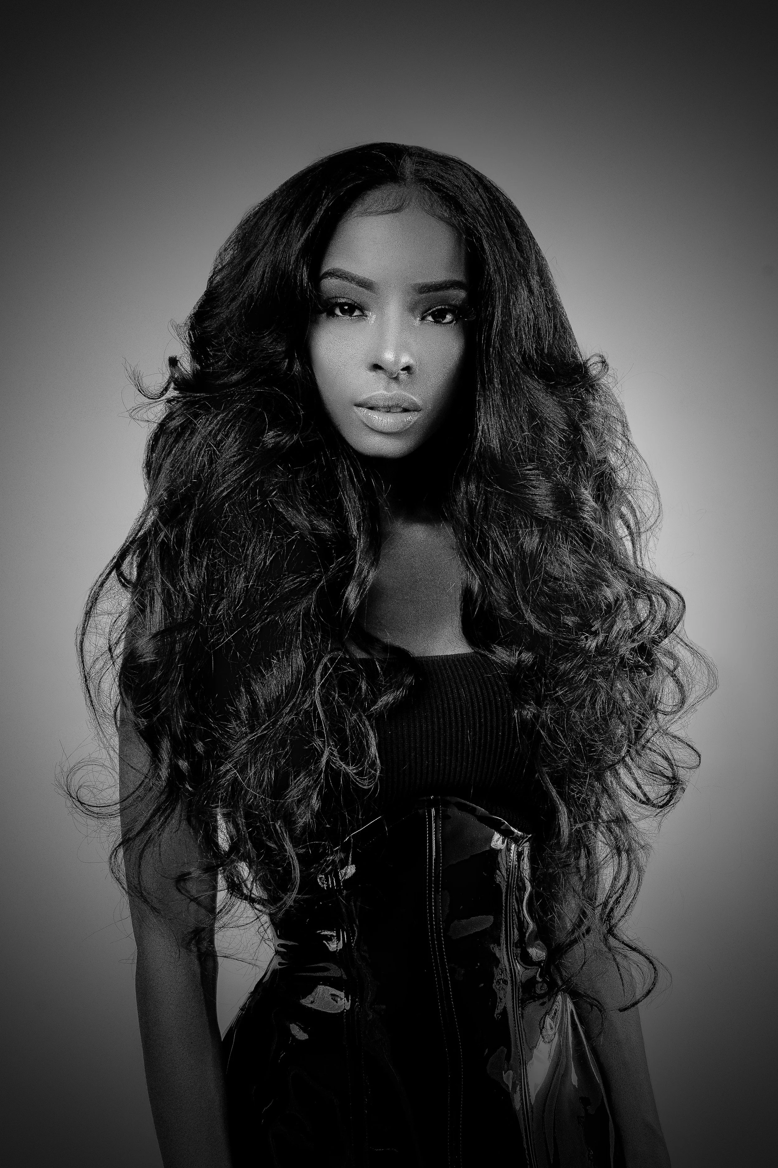 Black and white portrait of a woman with long, curly hair, wearing a sleeveless top and a jacket with a zipper.