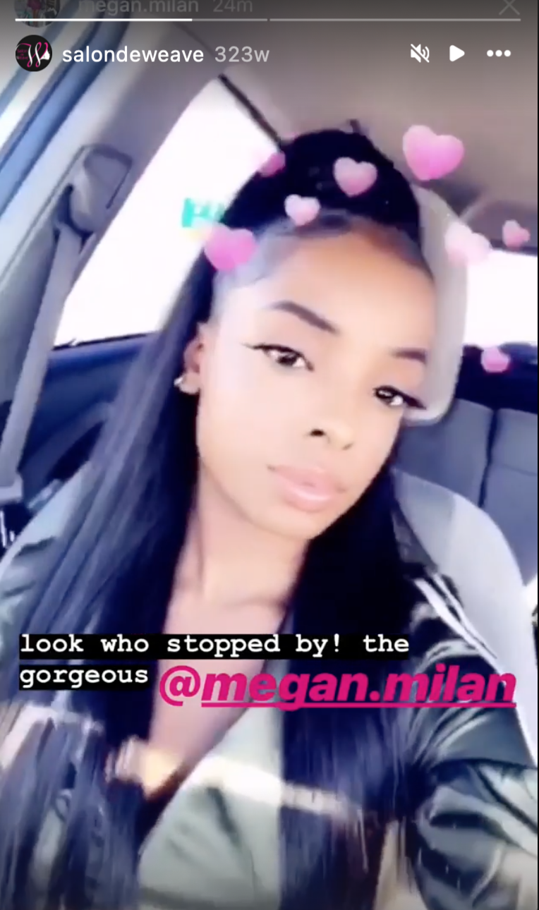 A woman with long dark hair and makeup sitting in a car, taking a selfie with a filter adding pink hearts around her head. The caption reads, "look who stopped by! the gorgeous @megan.milan."