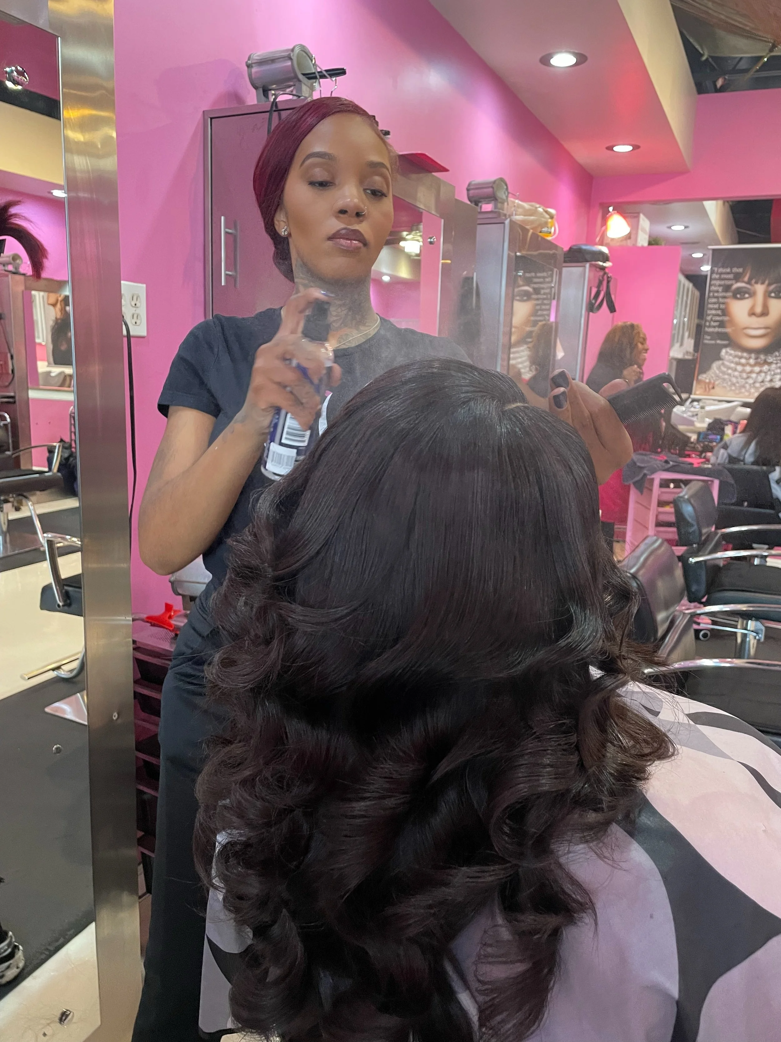 Salon de Weave stylist finishing a client’s long, voluminous curled hair extensions during a professional Refresh maintenance service.