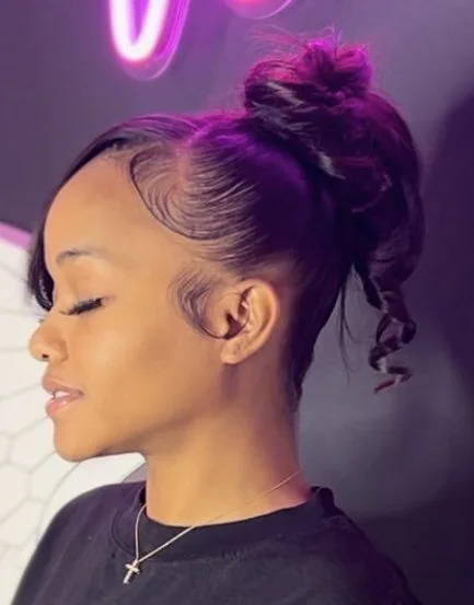 Side view of a client wearing a high bun with styled baby hairs and loose curls at Salon de Weave.