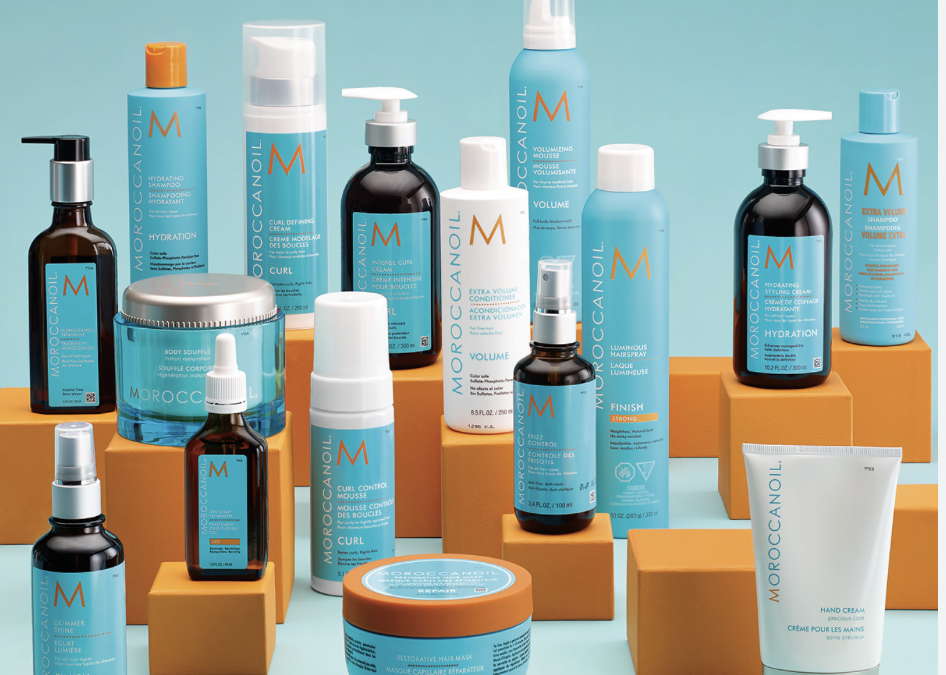 Collection of Moroccanoil hair and skin care products on orange and yellow stands against a blue background.