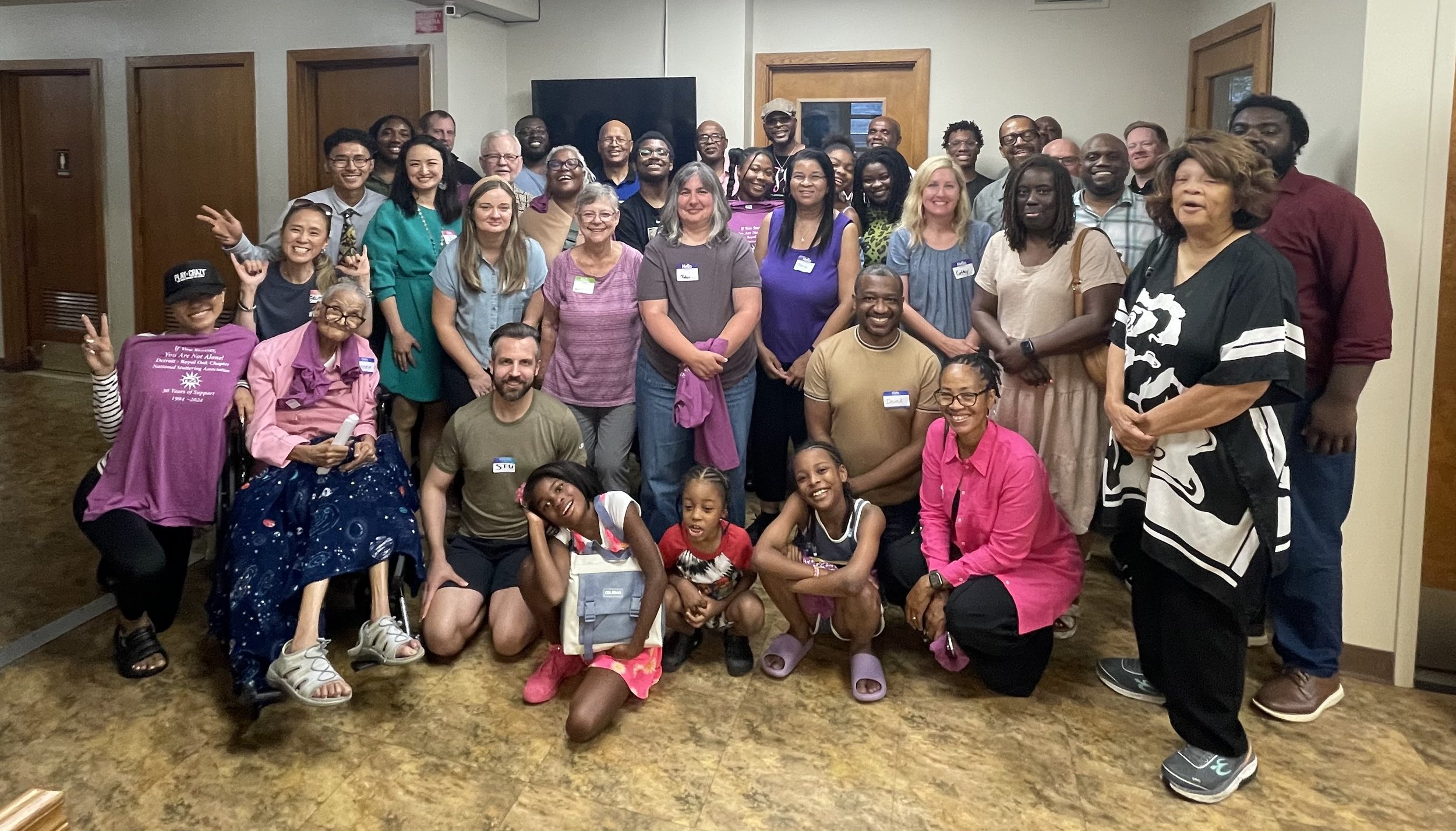 Group of diverse people gathered for a group photo indoors, smiling and posing together.