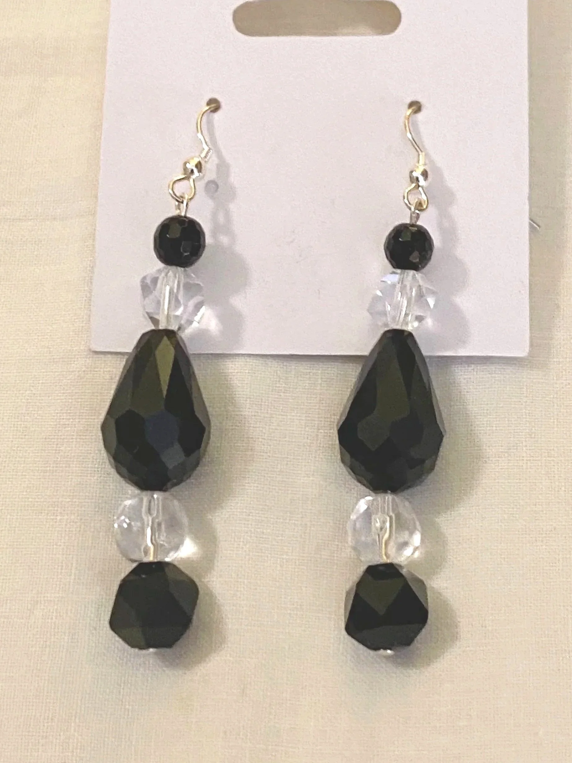 Pair of black and clear faceted drop earrings hanging from a white display card.