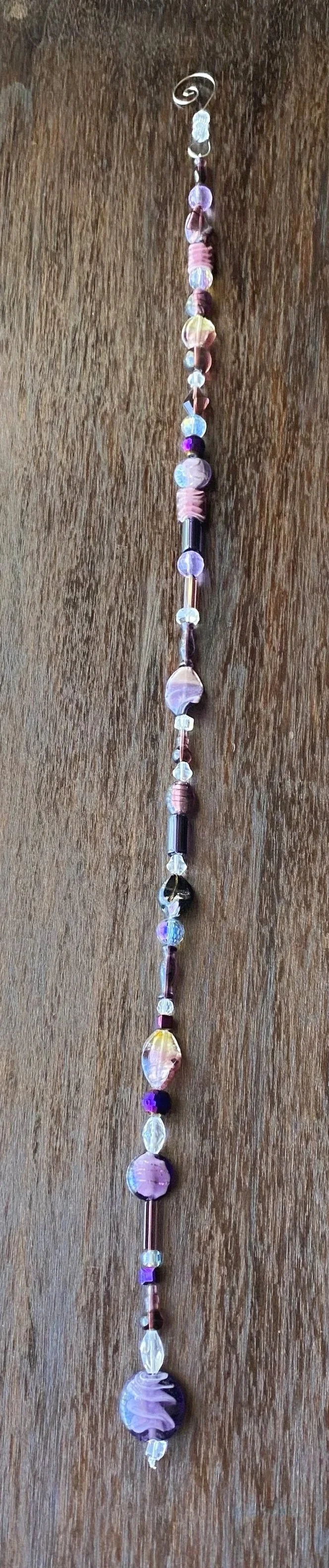 A beaded necklace with a variety of pink, purple, blue, and clear beads and a metal clasp, laid out on a wooden surface.