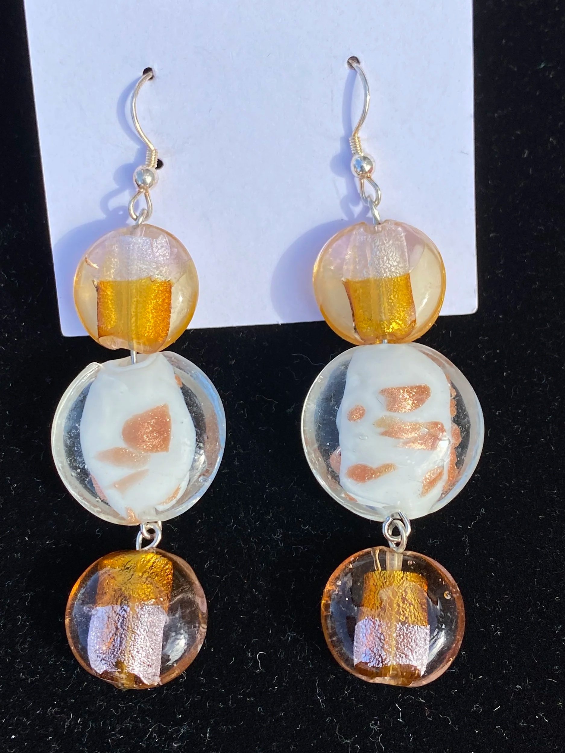 Pair of earrings with round amber-colored beads and clear teardrop-shaped pendants against a black background.