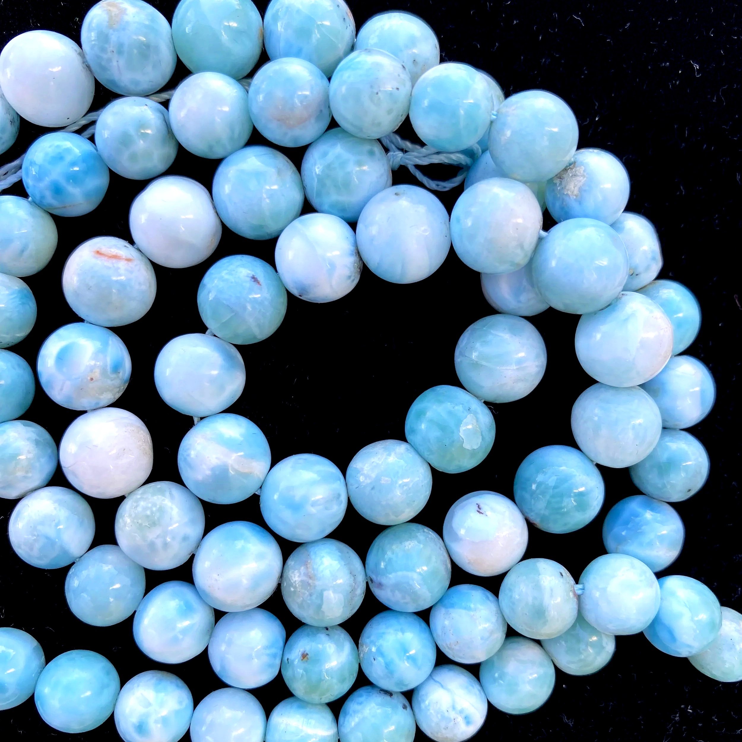 Close-up of a string of light blue, slightly iridescent beads on a black background.
