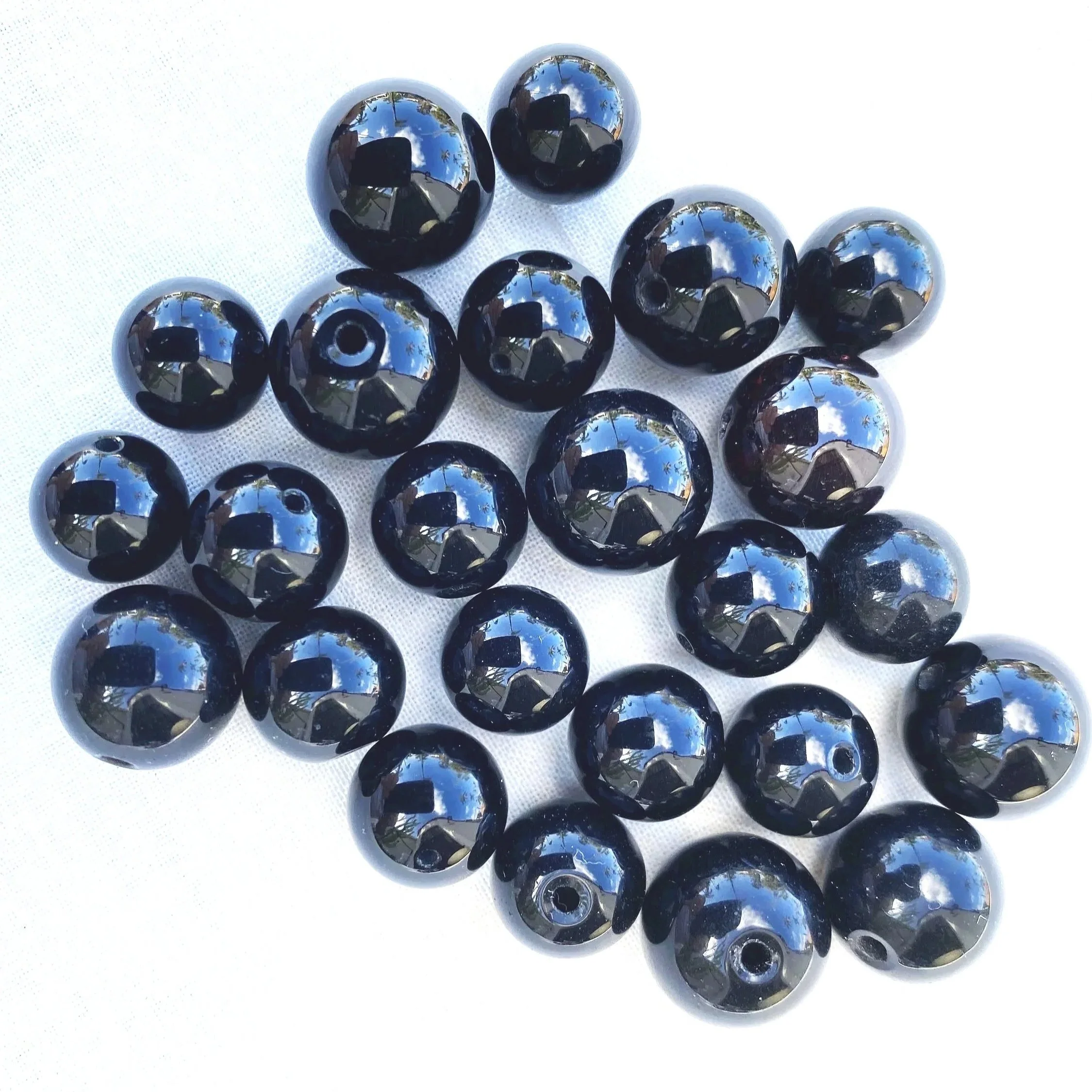 A collection of black polished onyx beads with reflective surfaces, arranged on a white background.