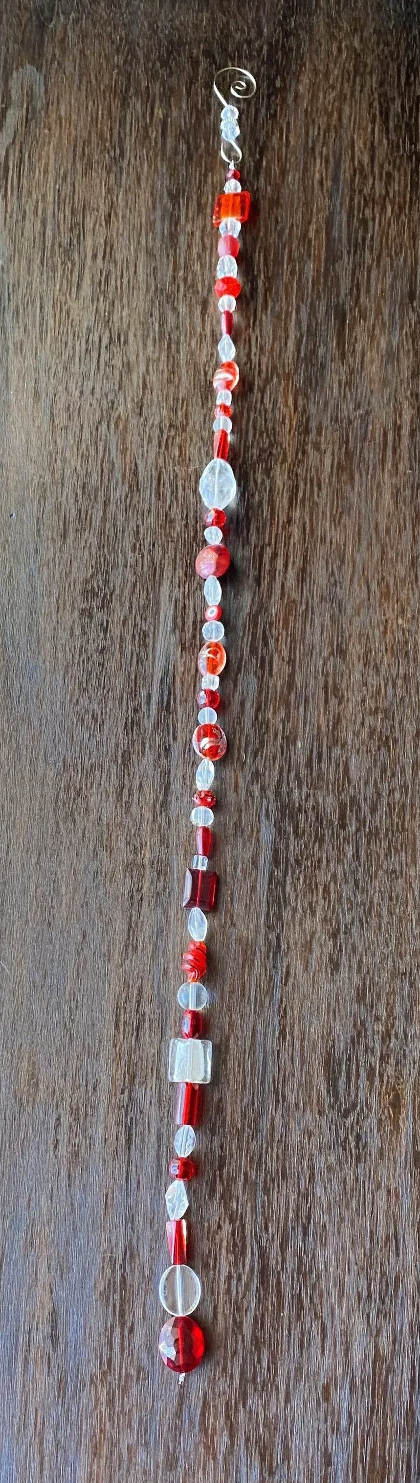 A string of various red and clear glass beads of different shapes and sizes laid out on a wooden surface.