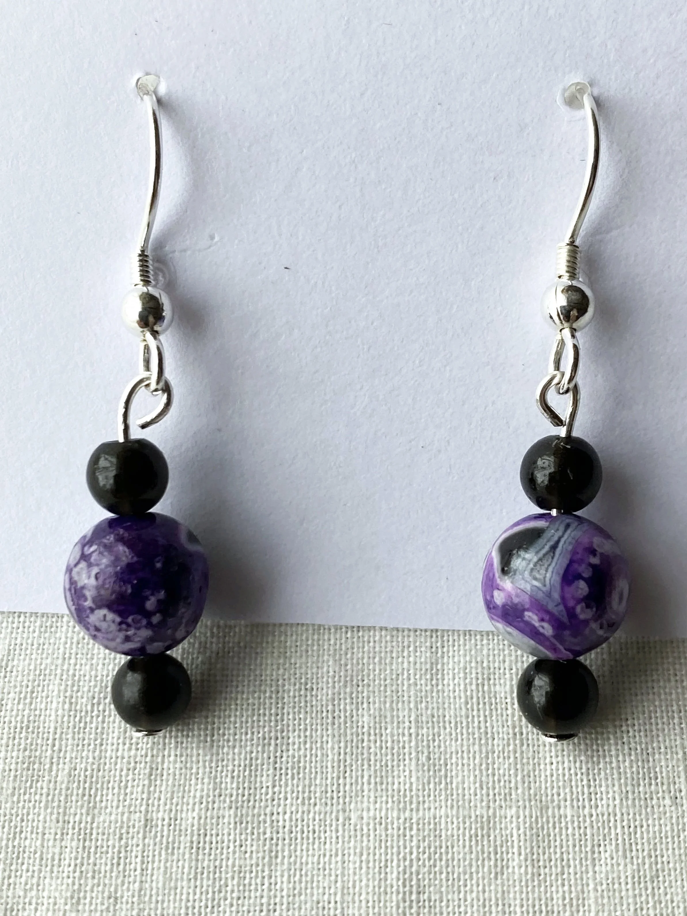 Pair of beaded earrings with purple, black, and gray beads on a white background.