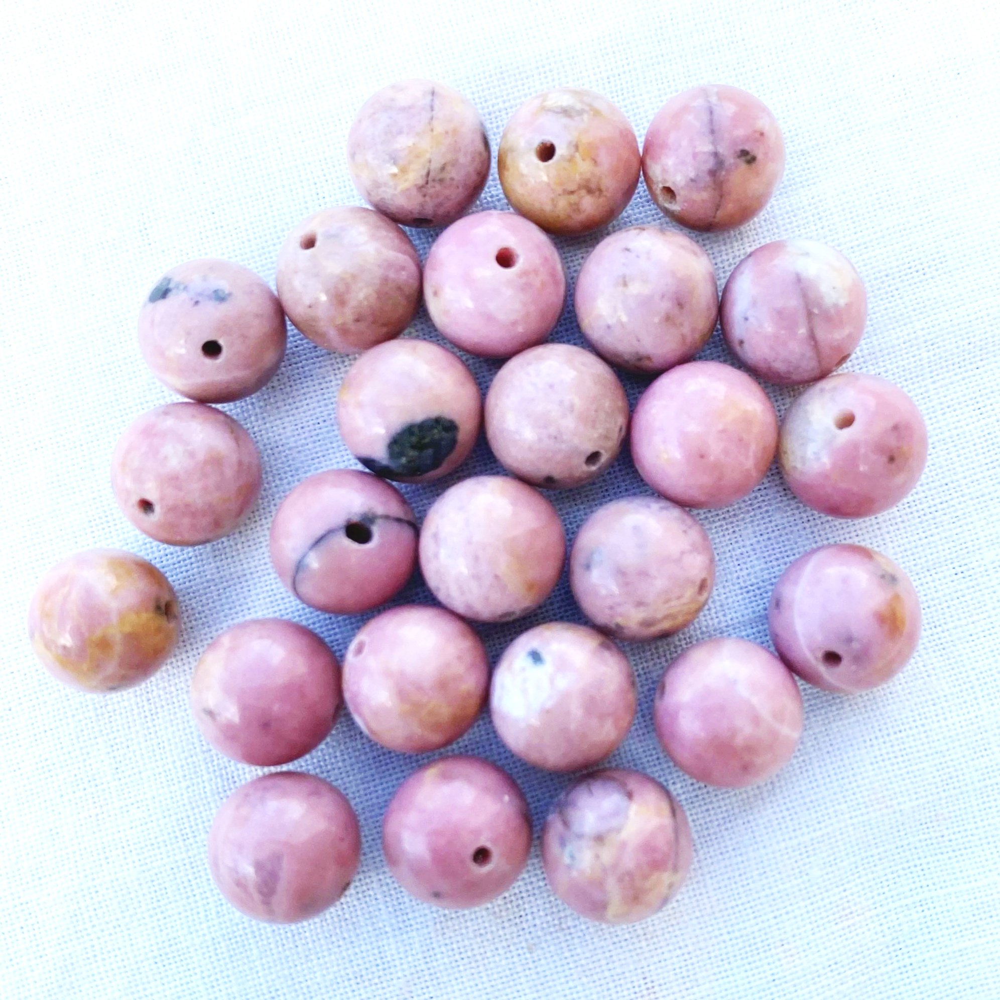 Close-up of pinkish-beige round beads with holes in the center, arranged on a textured white surface.