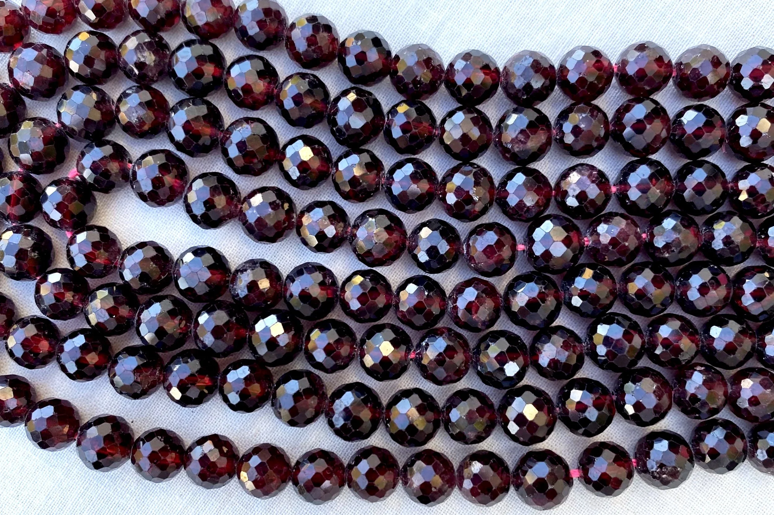 Multiple strands of dark red, iridescent, faceted beads arranged on a white surface.