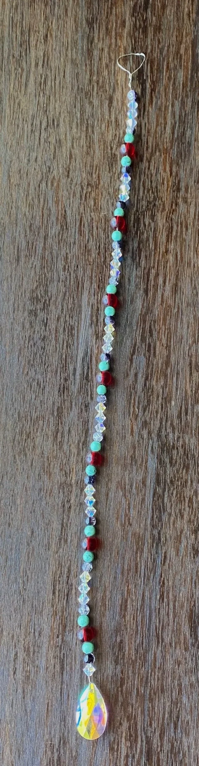 String of colorful beads and a teardrop-shaped pendant on a string, hung vertically against a wooden background.