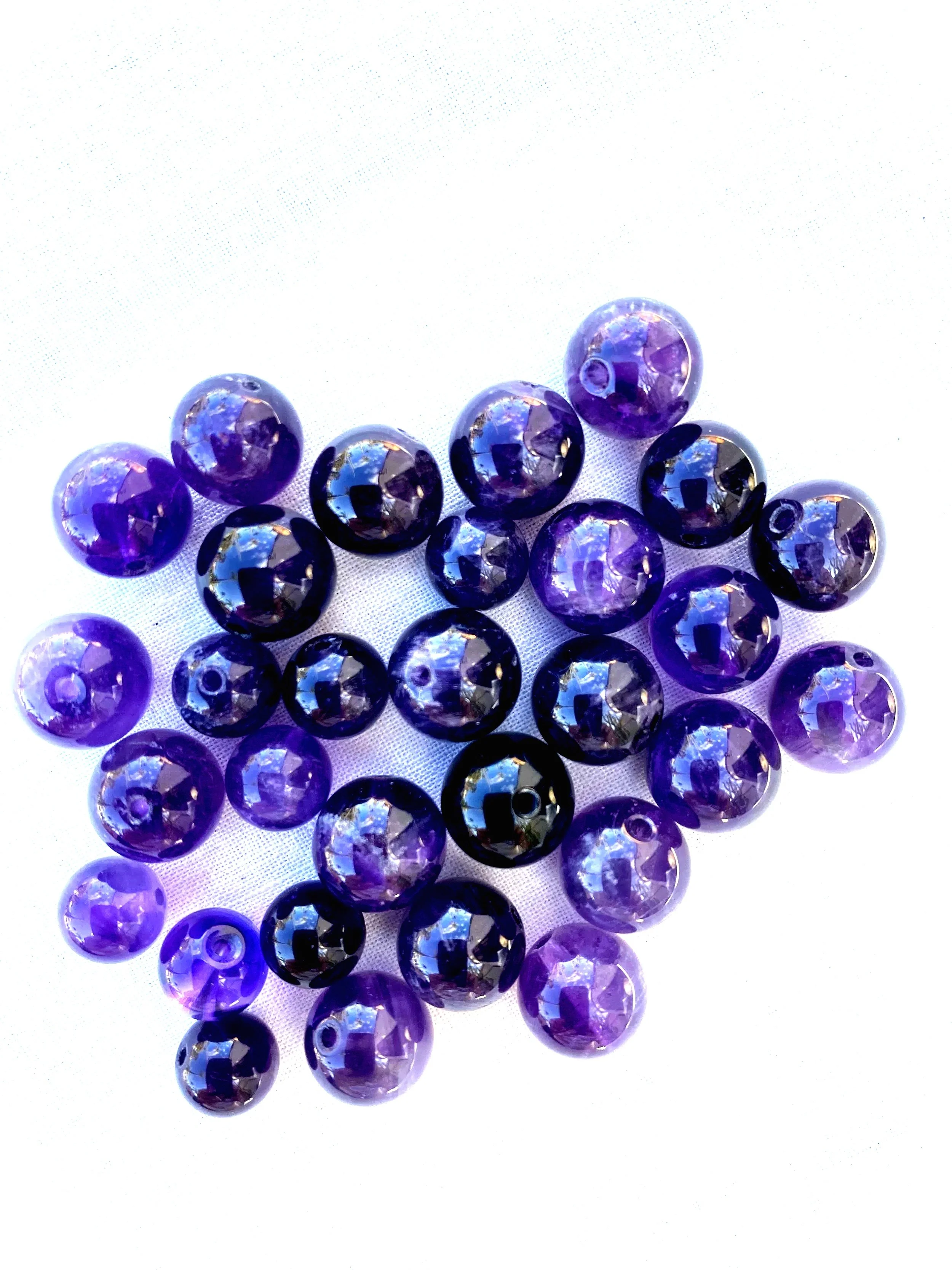 Multiple purple and black glass beads arranged on a white surface.
