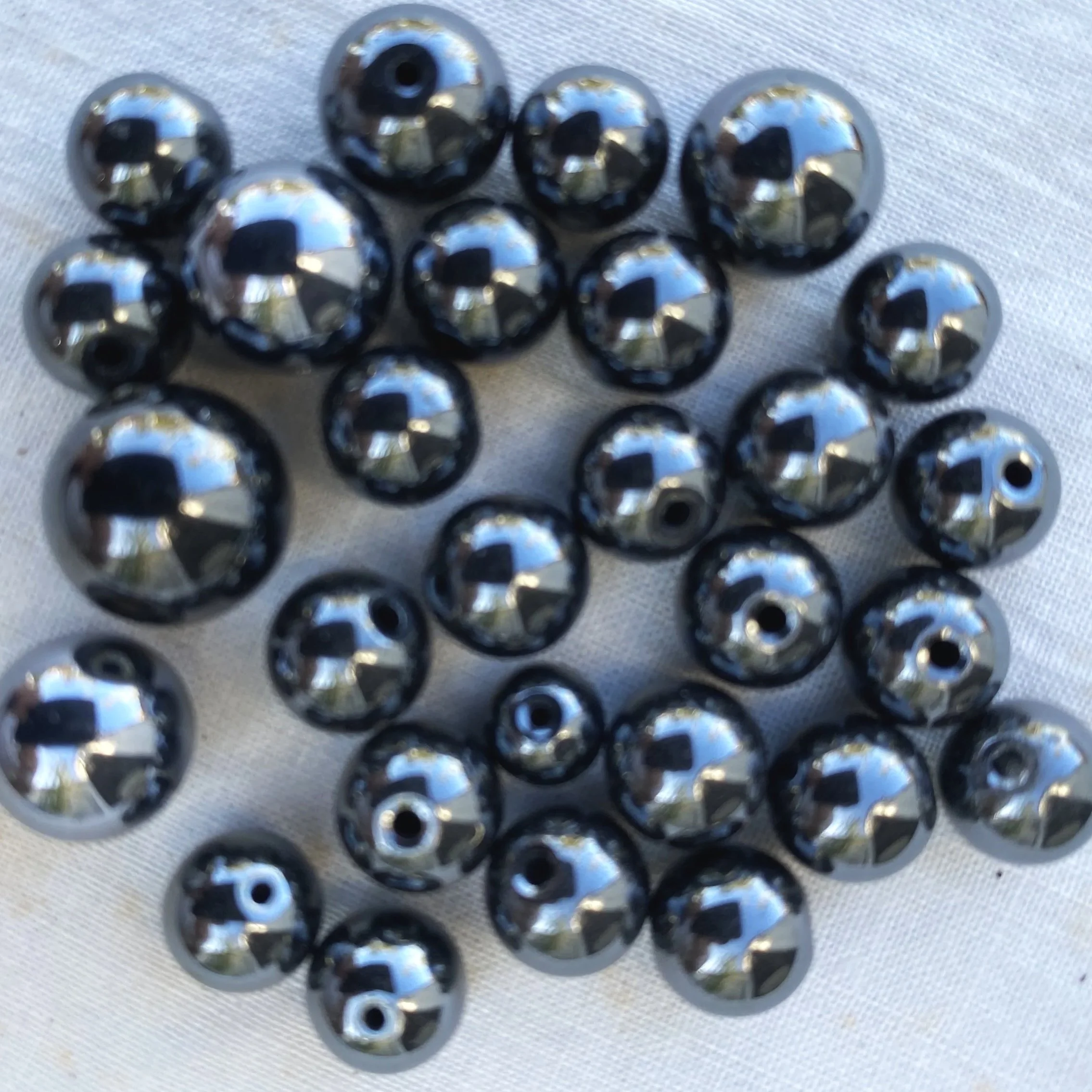 A close-up of multiple shiny round beads, arranged on a light-colored fabric surface.