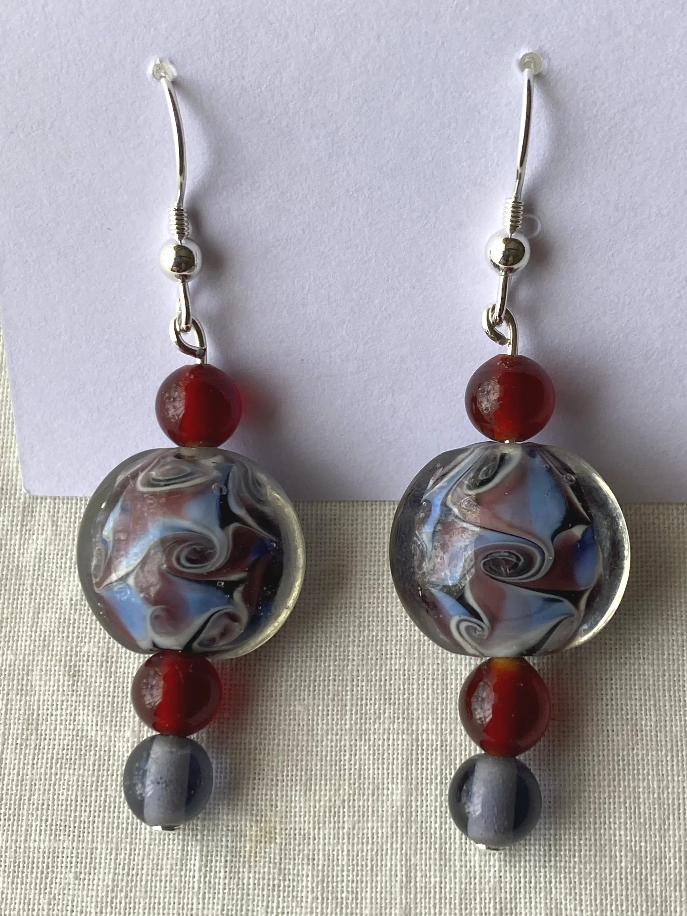 Pair of colorful glass dangle earrings on white background with red, black, and white swirled patterns and silver hooks.