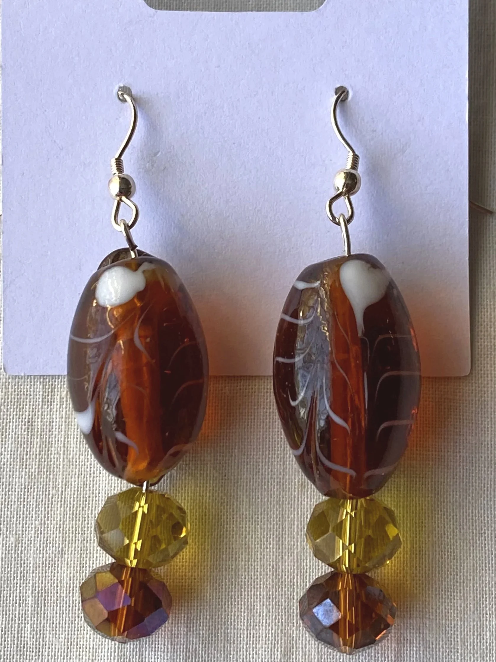 Pair of dangling earrings with amber-colored glass beads, gold-colored wire, and large faceted gold beads at the bottom.