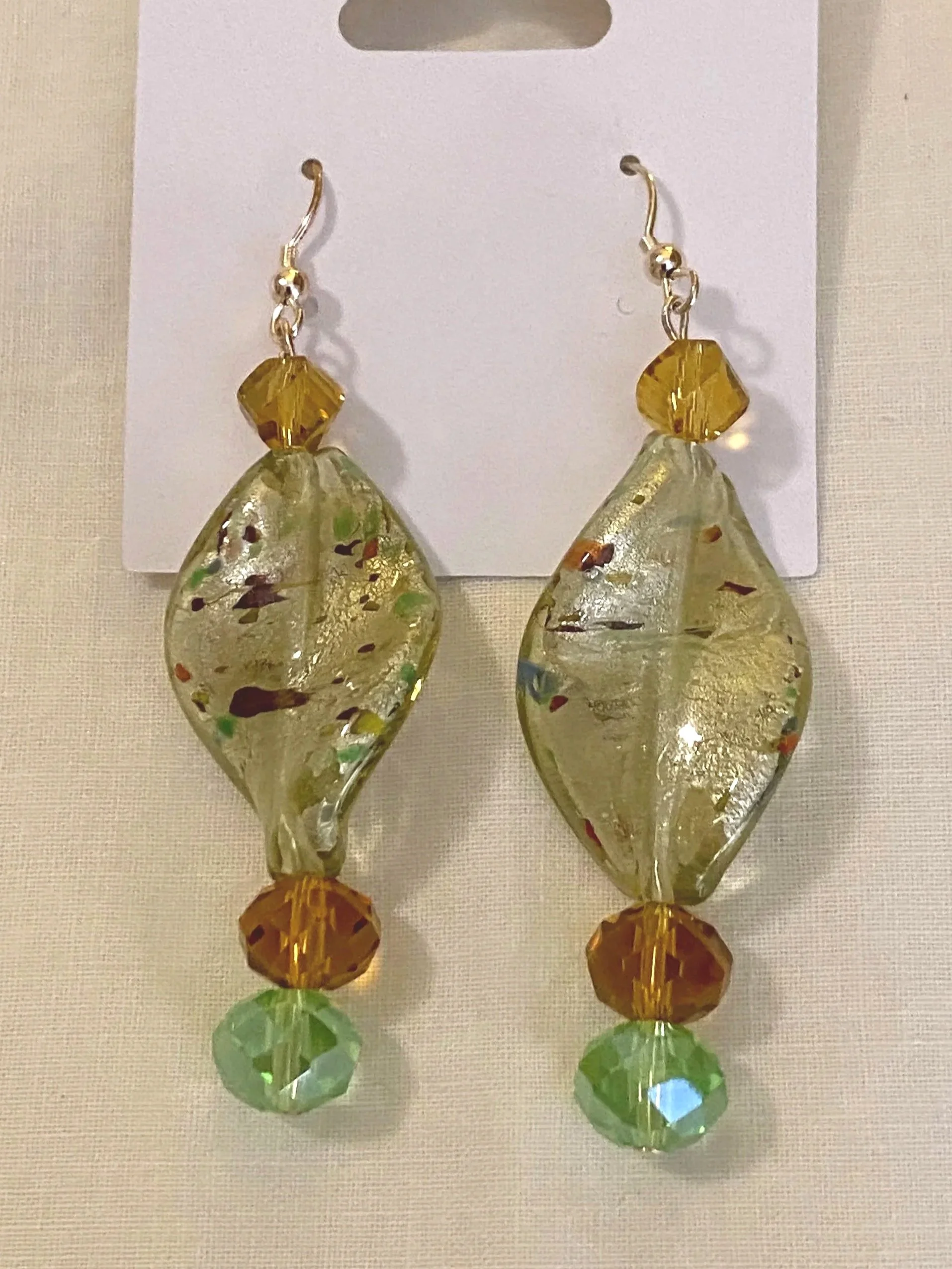 Colorful glass beaded earrings with faceted green and brown beads, hanging on a white display card.