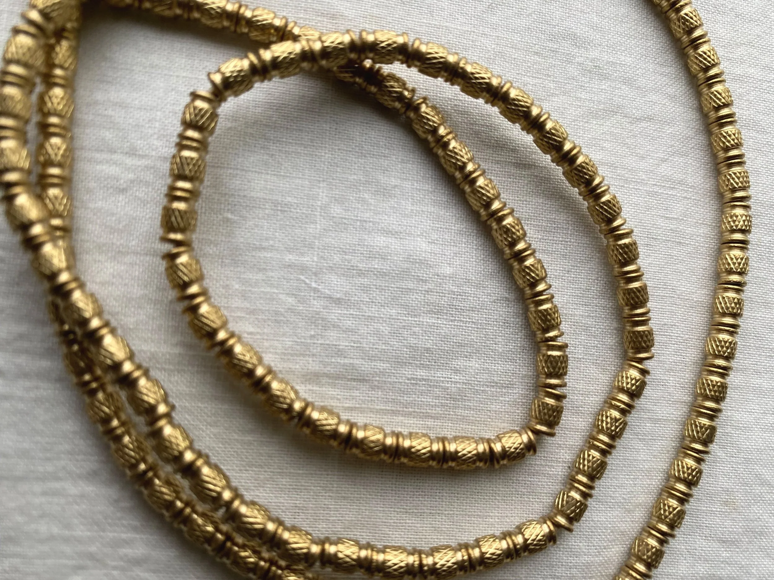 Close-up of three gold beads with intricate textured designs on a white fabric background.