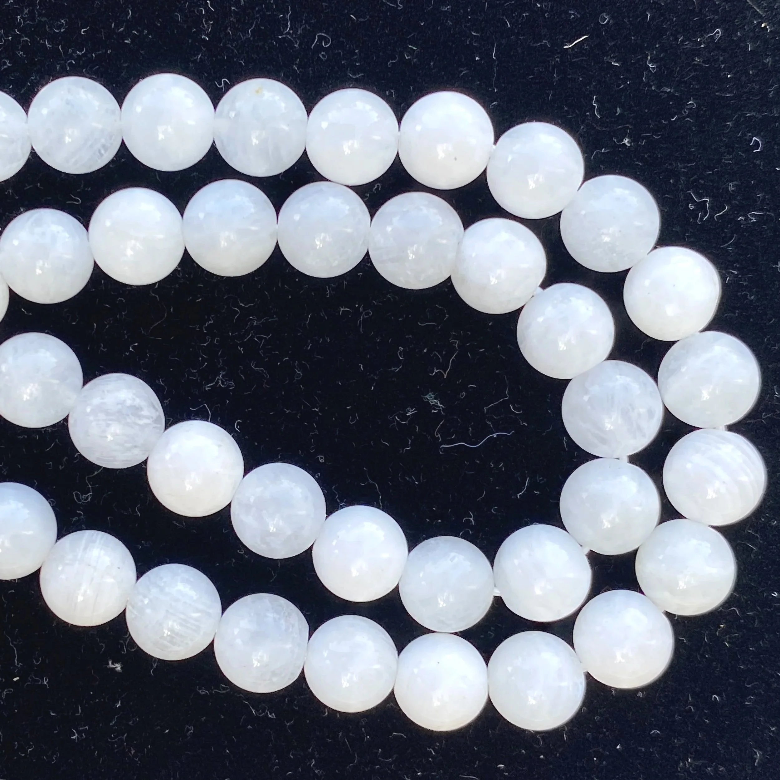 Close-up of white spherical moonstone beads arranged in a curve on a black textured background.