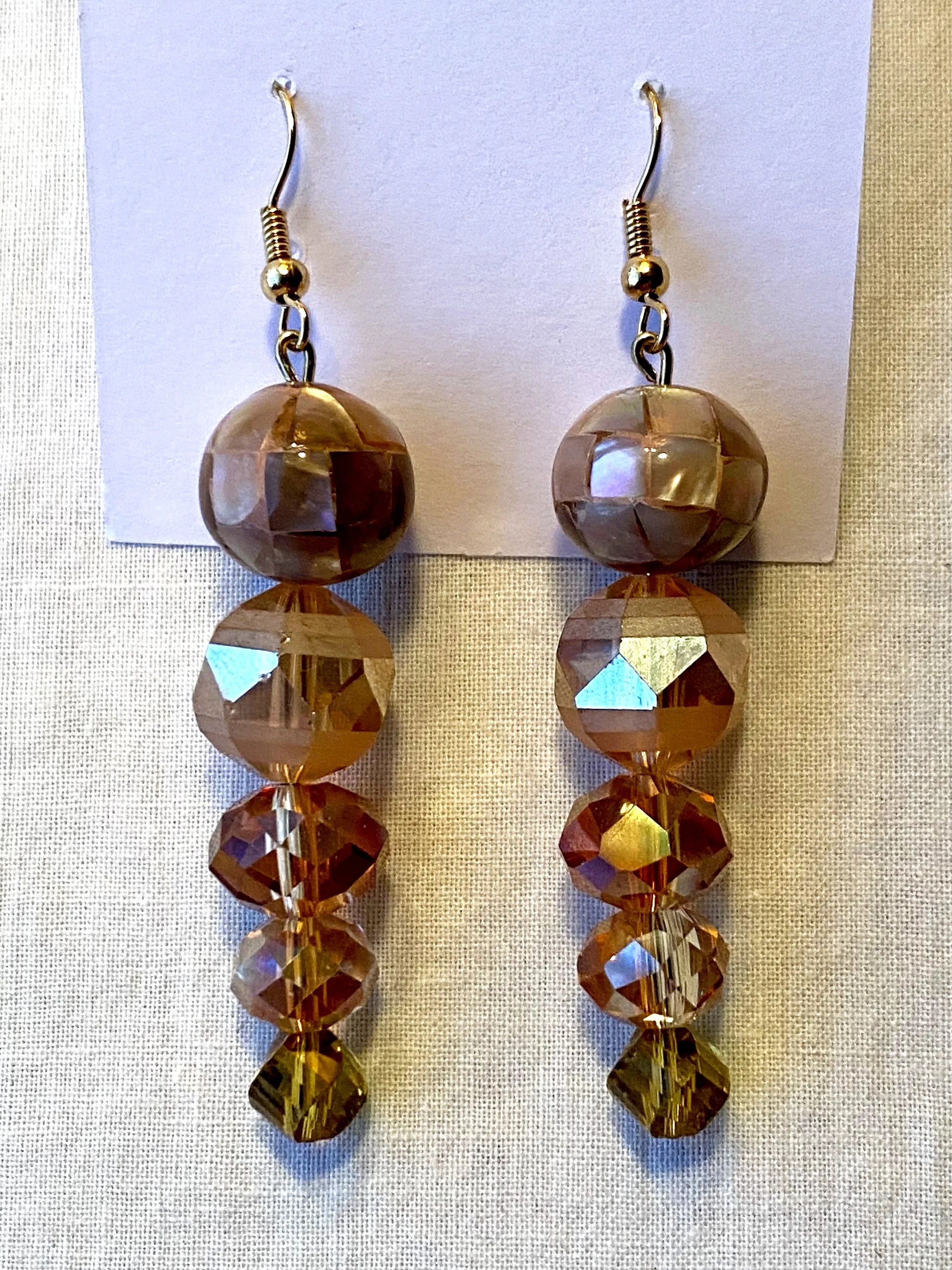 A pair of gold and bronze dangling earrings with large faceted beads and crystals, displayed on a white card.