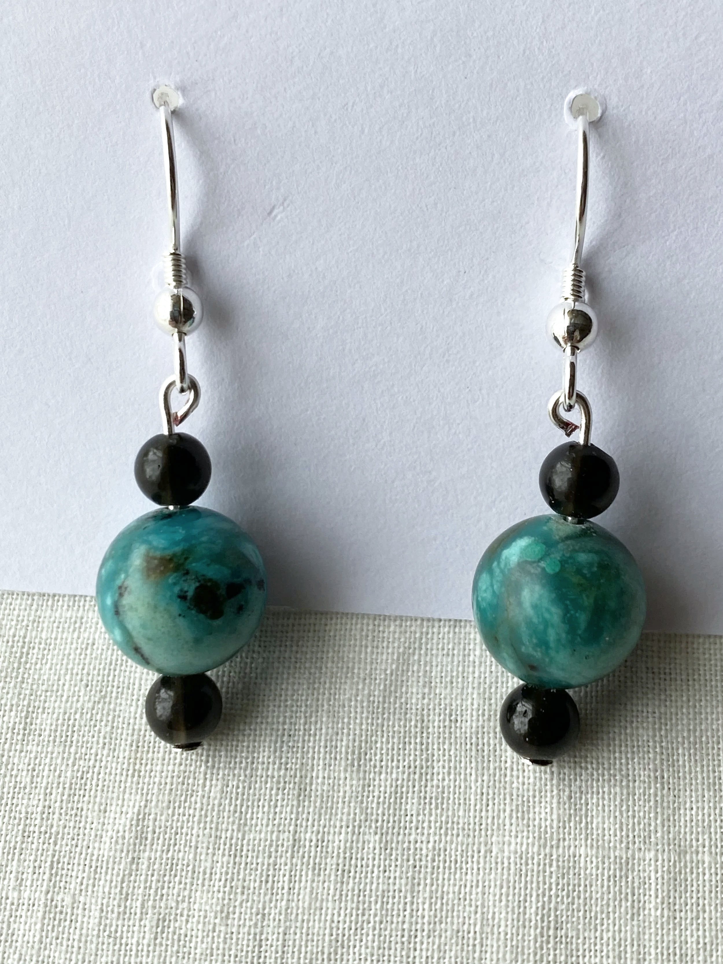 Pair of dangling earrings with black and turquoise beads on a white surface.