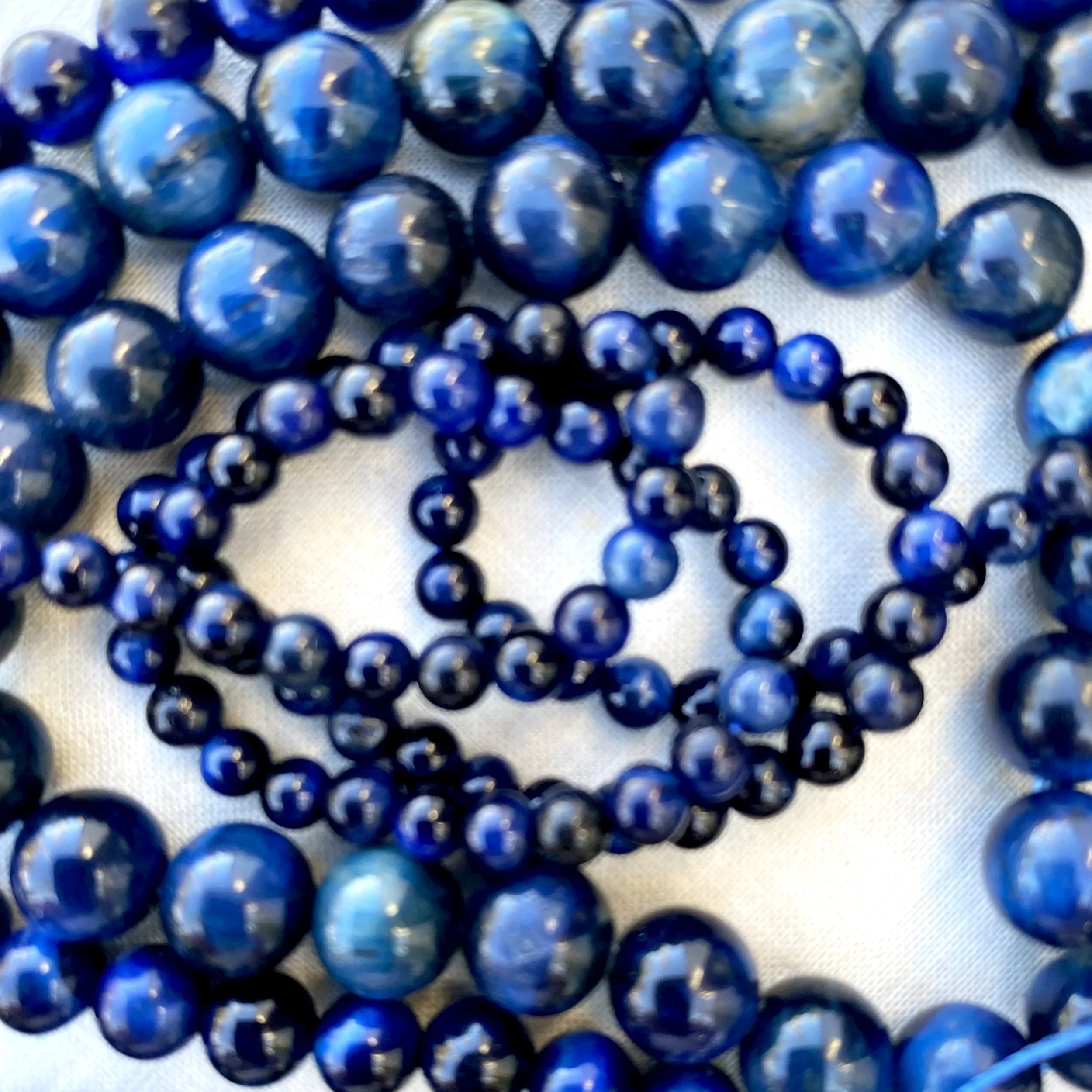 Close-up of multiple blue tigers eye beads with reflective surfaces arranged on a light background.