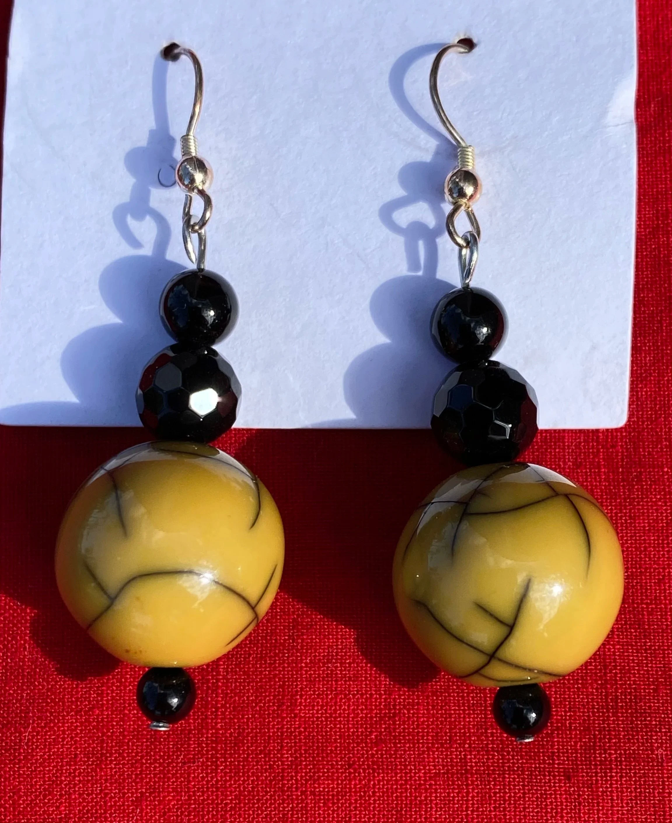 A pair of black and yellow glass earrings with a marbled pattern, hanging on hooks against a white and red background.