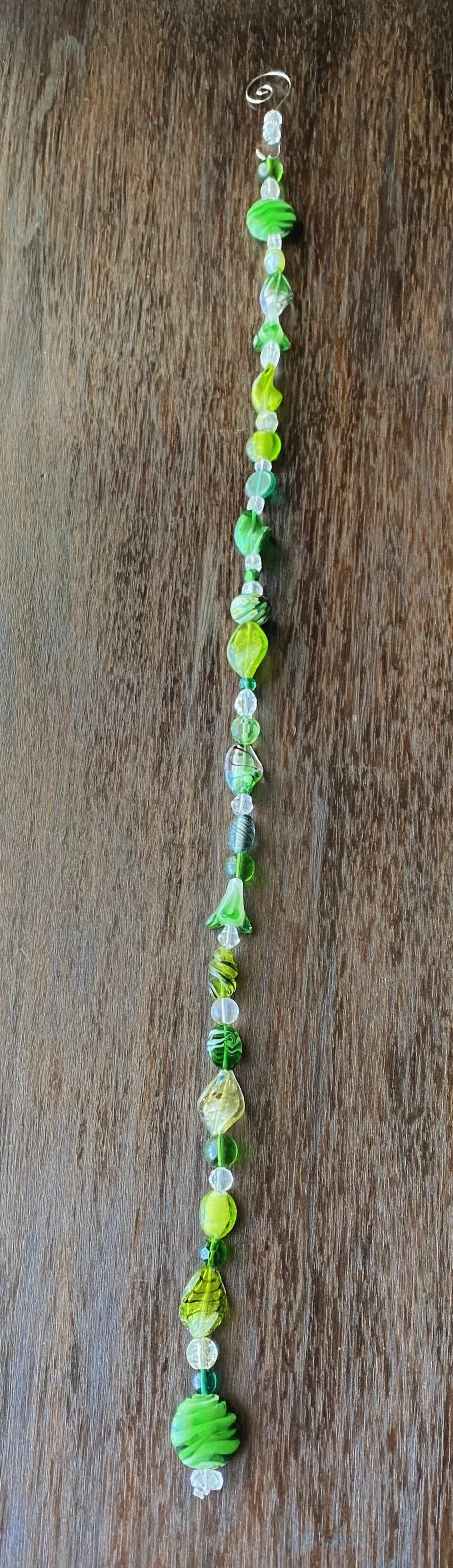 A vertical string of various green, white, and clear glass beads on a wooden surface.